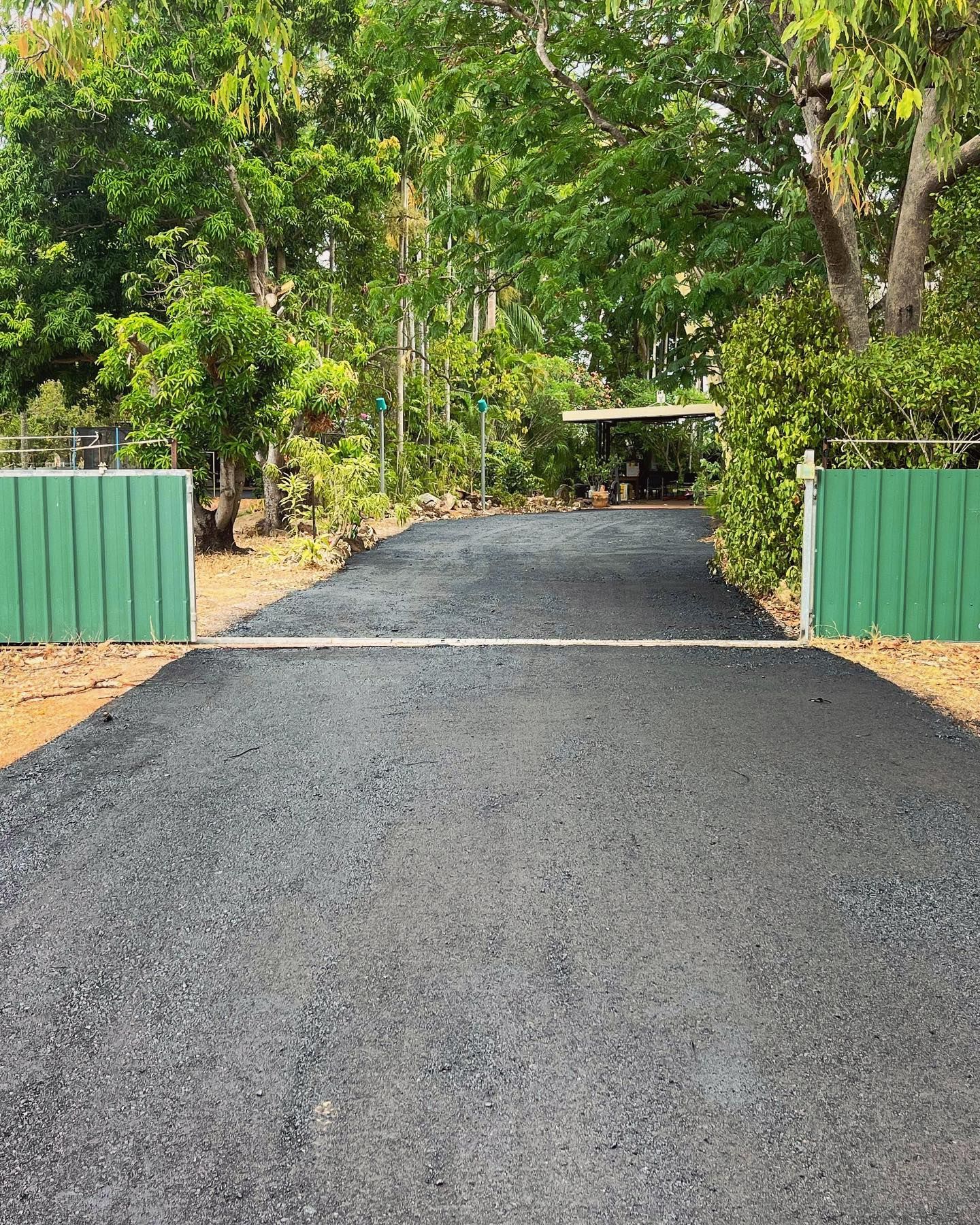 Black Driveway Sheet In The Garden And Green Grass With Cement Path Contrasting With The Bright Green Lawns And Shrubs, Trees And Morning Sun Garden Landscape Design — Rural & Commercial Landscaper in Humpty Doo, NT