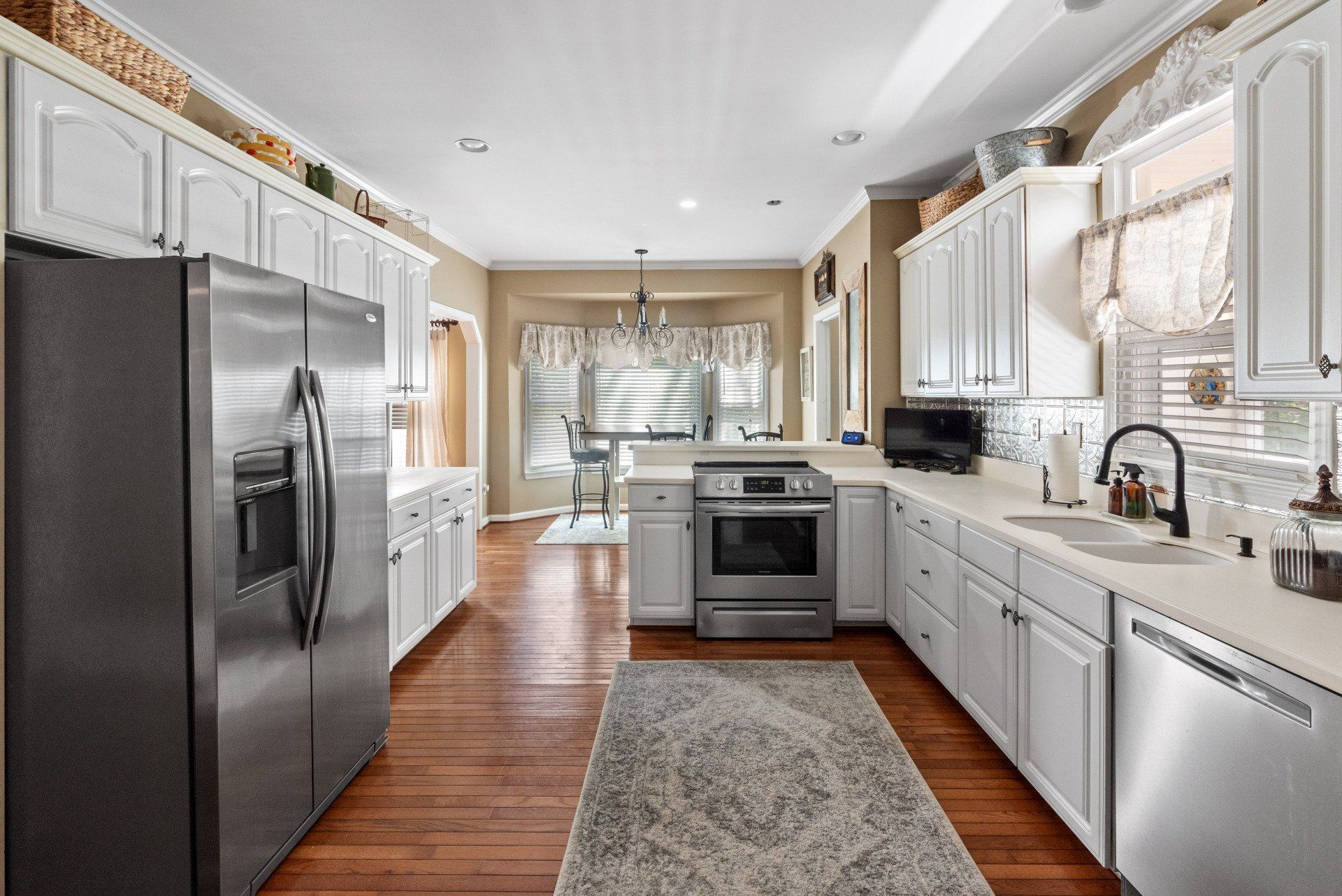 Bright kitchen with white cabinets, stainless steel appliances, and wood floor.