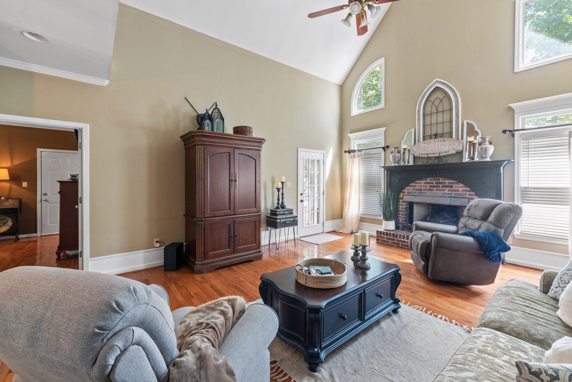 Living room with high ceiling, fireplace, wooden floor, and furniture.