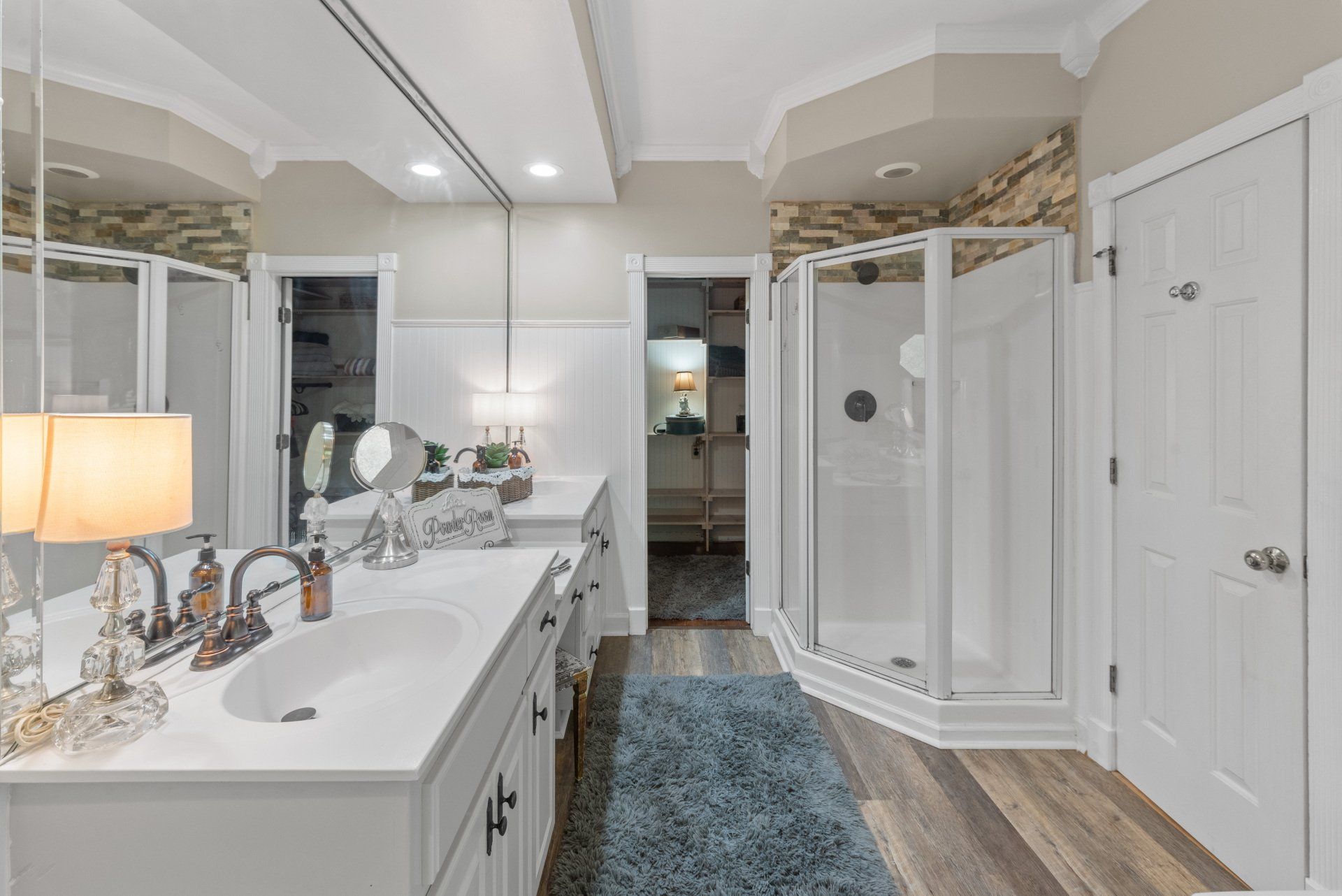 Bathroom with white vanity, shower, and doors; wood-look flooring and a blue rug.