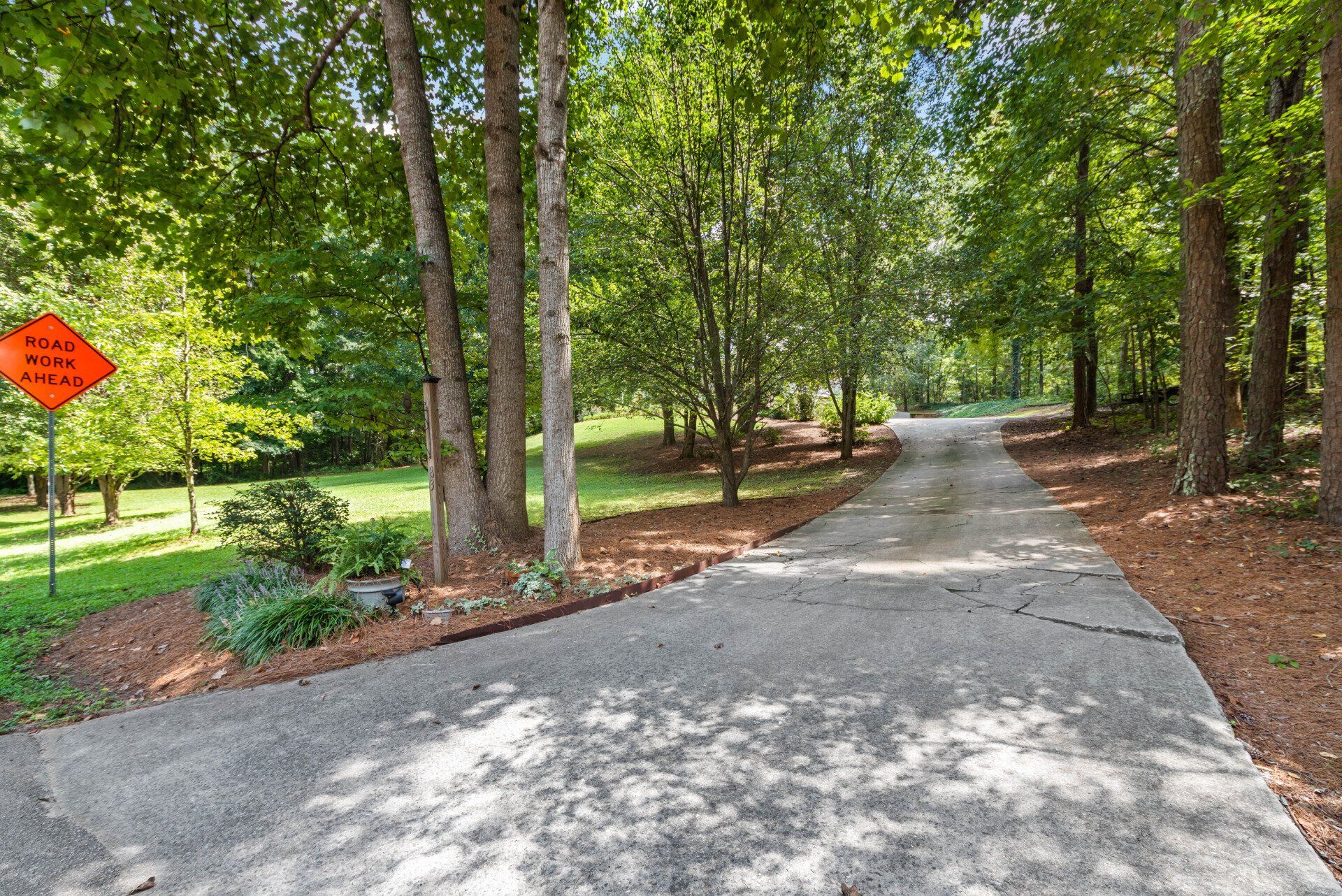Driveway curves through trees with a construction sign on the left.