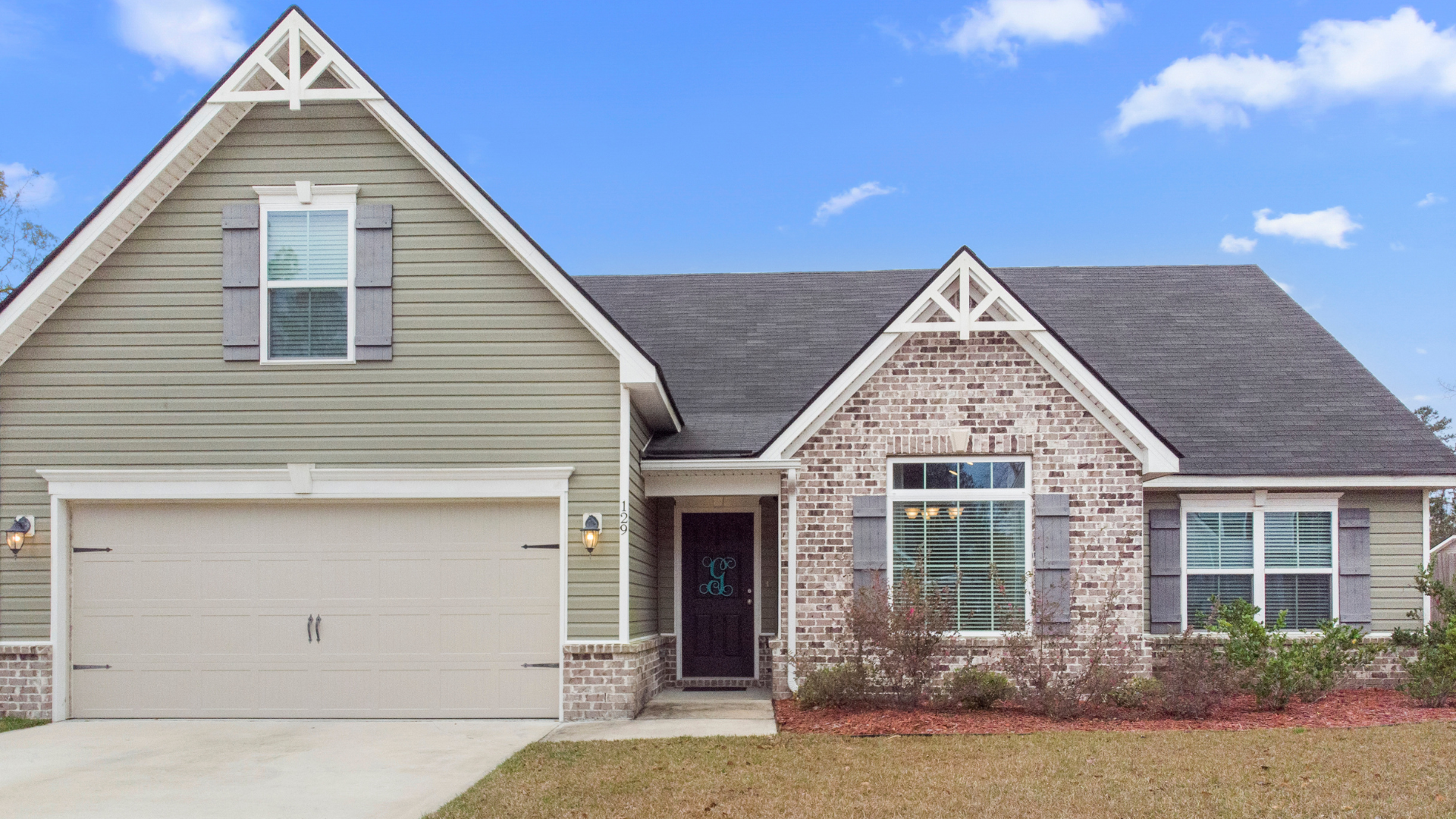 A light green house with a gray roof and brick accents on a sunny day.