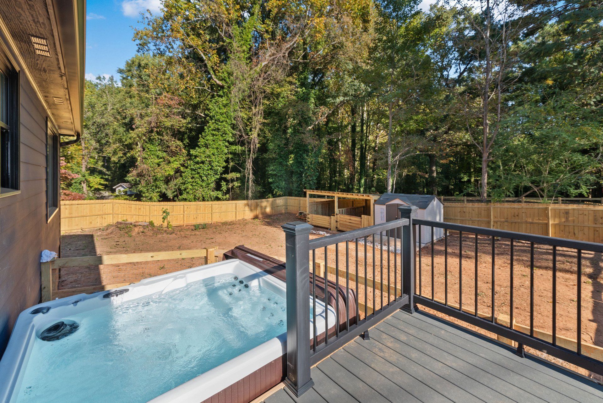 Backyard with hot tub, deck, and shed; surrounded by a wooden fence and trees.