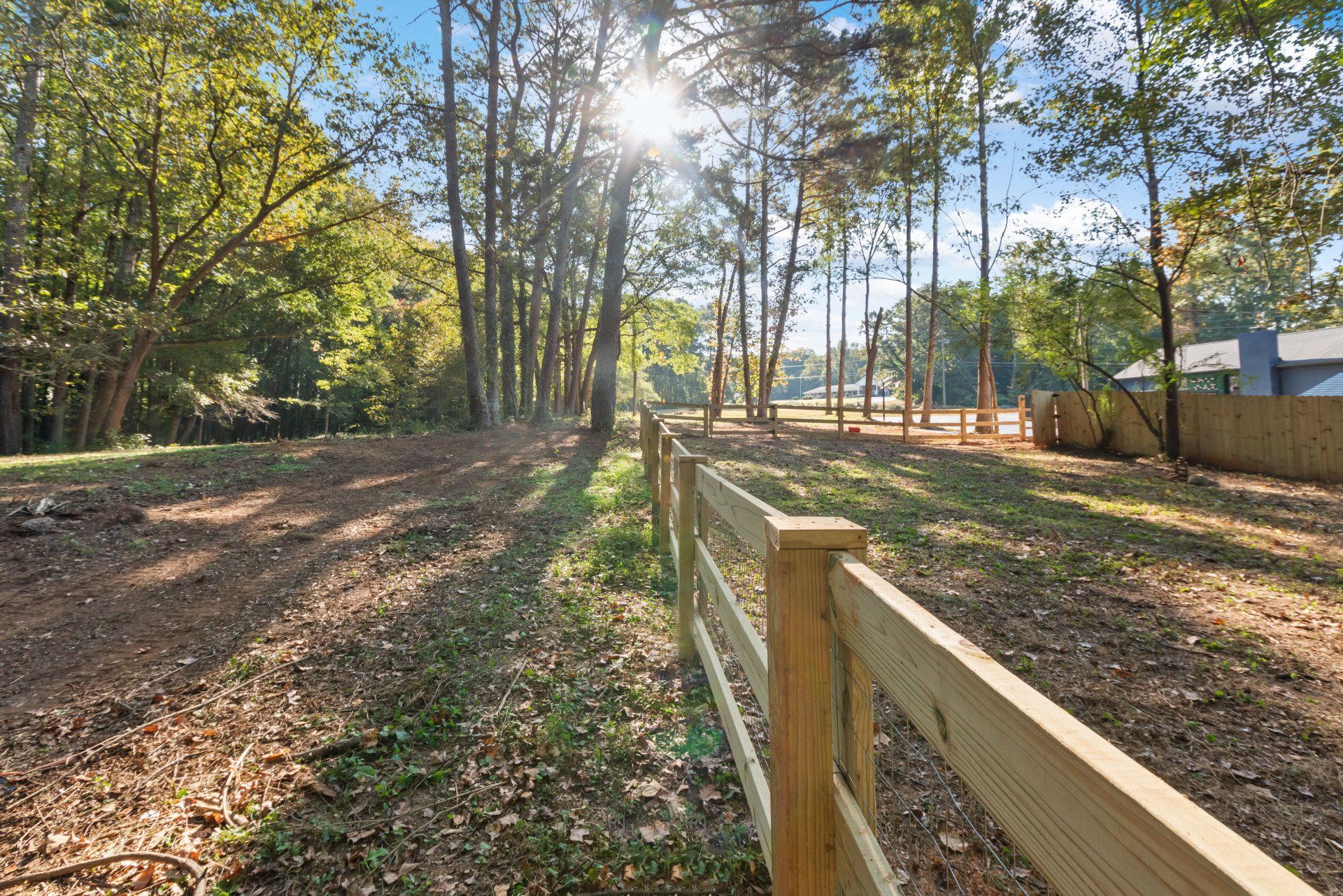 Wooden fence lines a clearing with trees and sunlight.