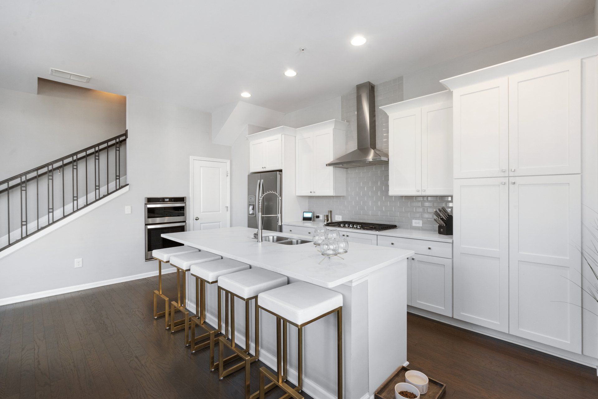 Modern kitchen with white cabinets, island with stools, stainless steel appliances, and dark wood floors.