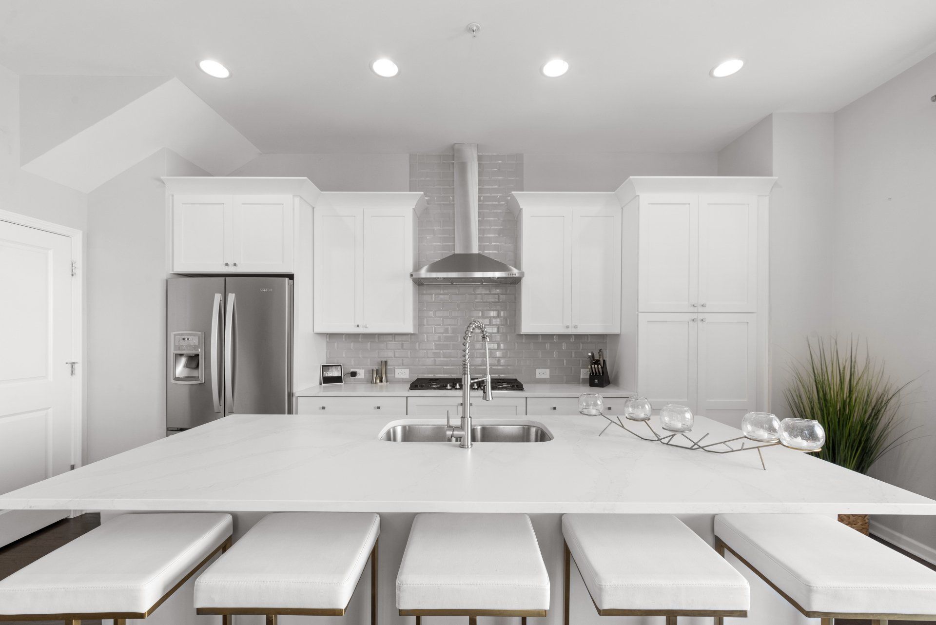 White modern kitchen with island, seating, and stainless steel appliances.