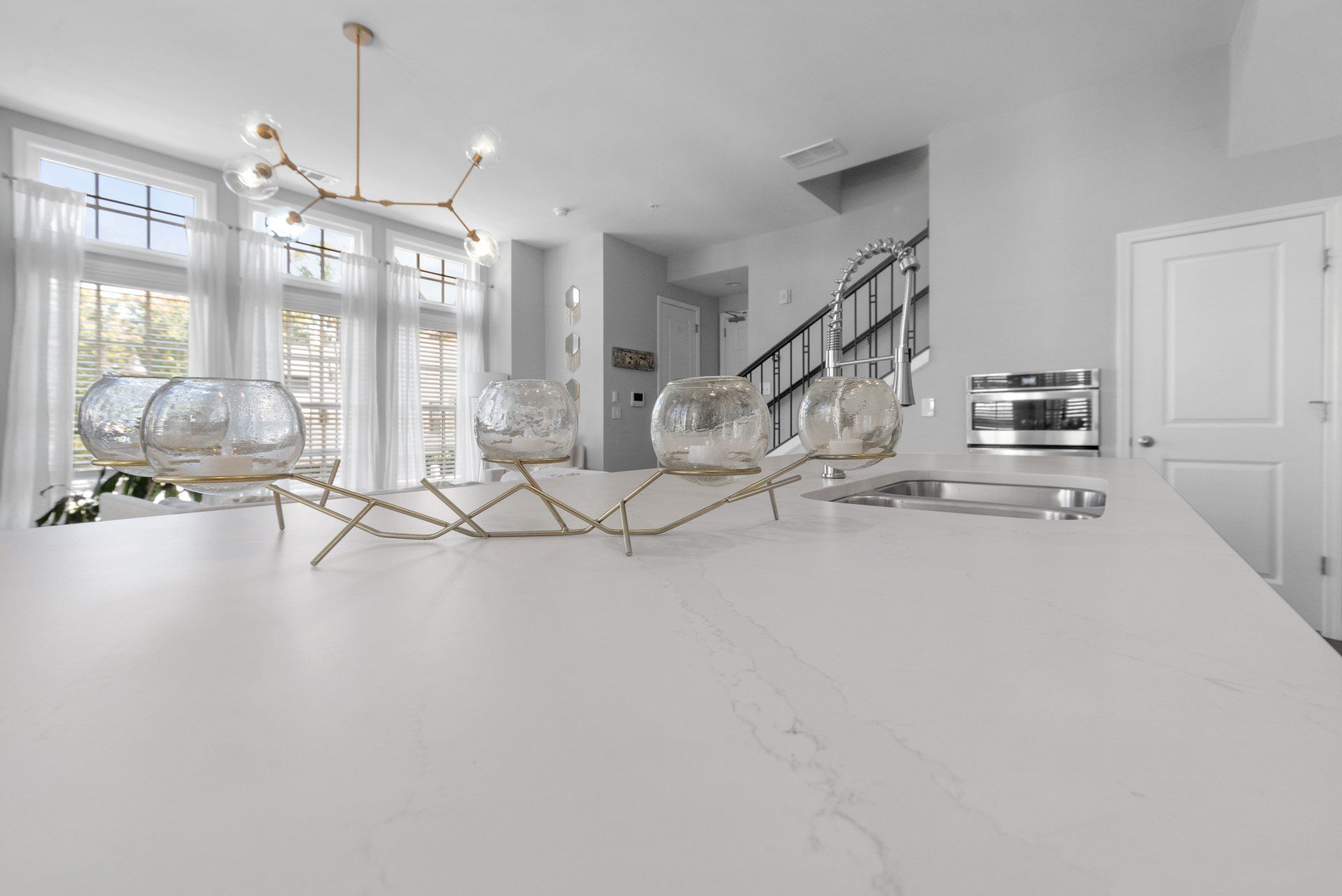 Bright white kitchen interior with marble countertop, glass globe decor, and a gold chandelier.