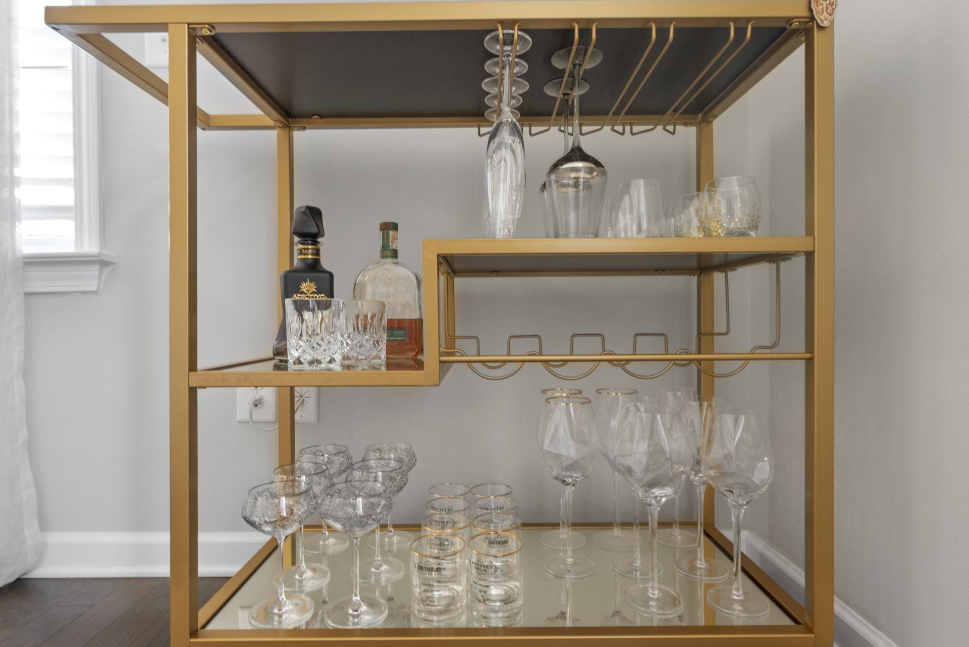 Gold bar cart with drinks and glasses on shelves.