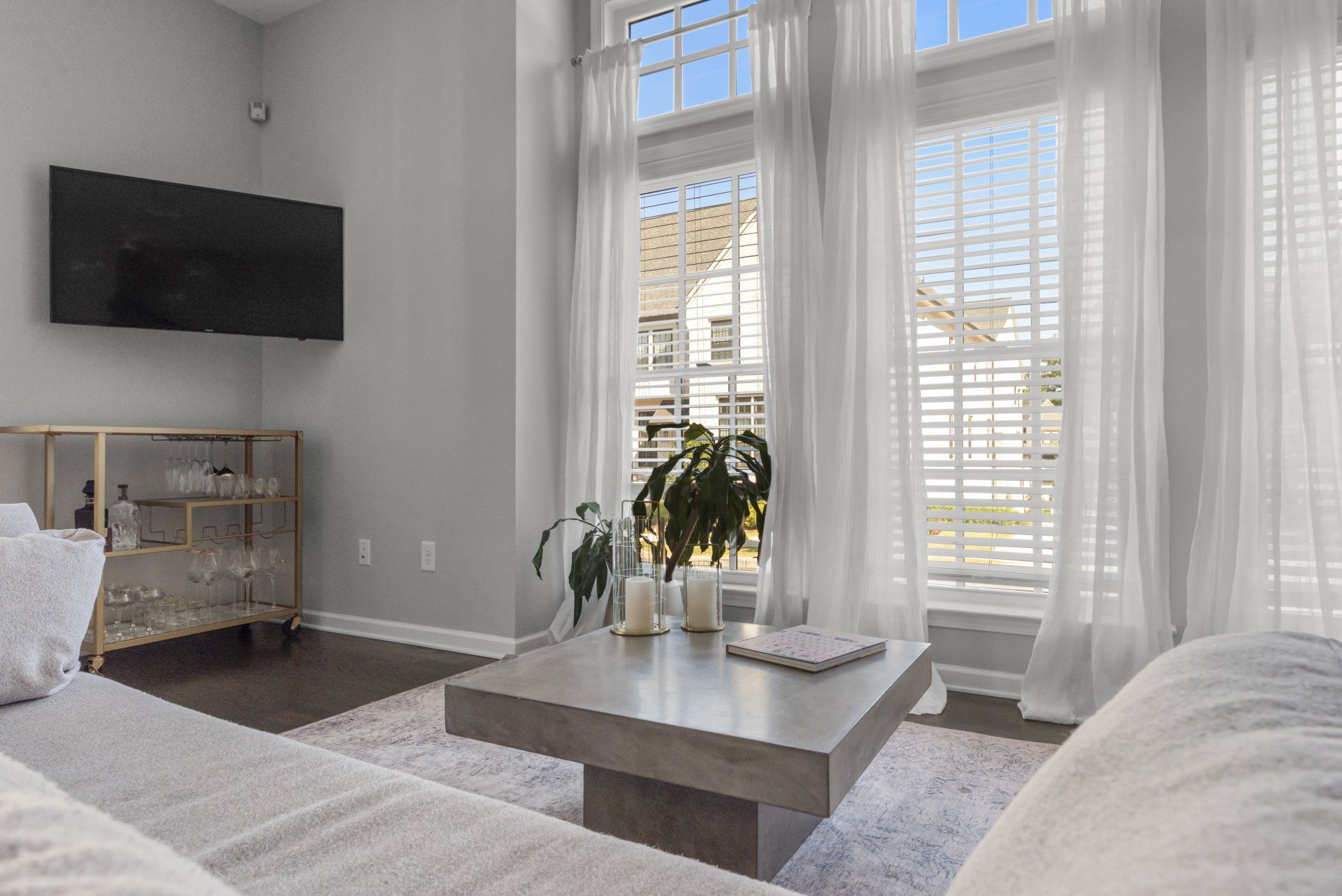 Living room with large windows, sheer white curtains, and a concrete coffee table.