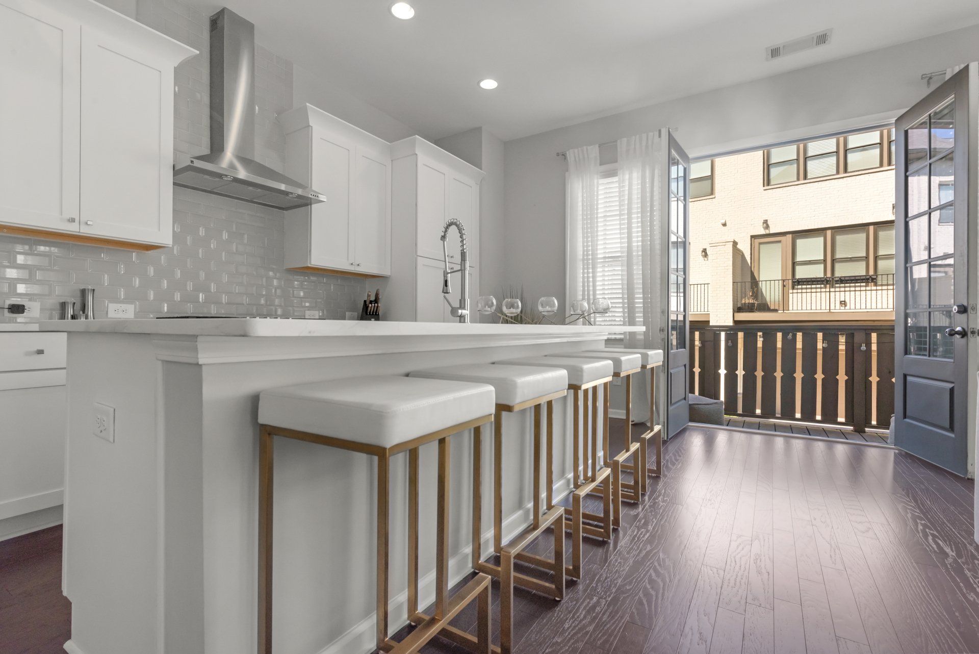 White kitchen with island, bar stools, and open doors to a balcony.