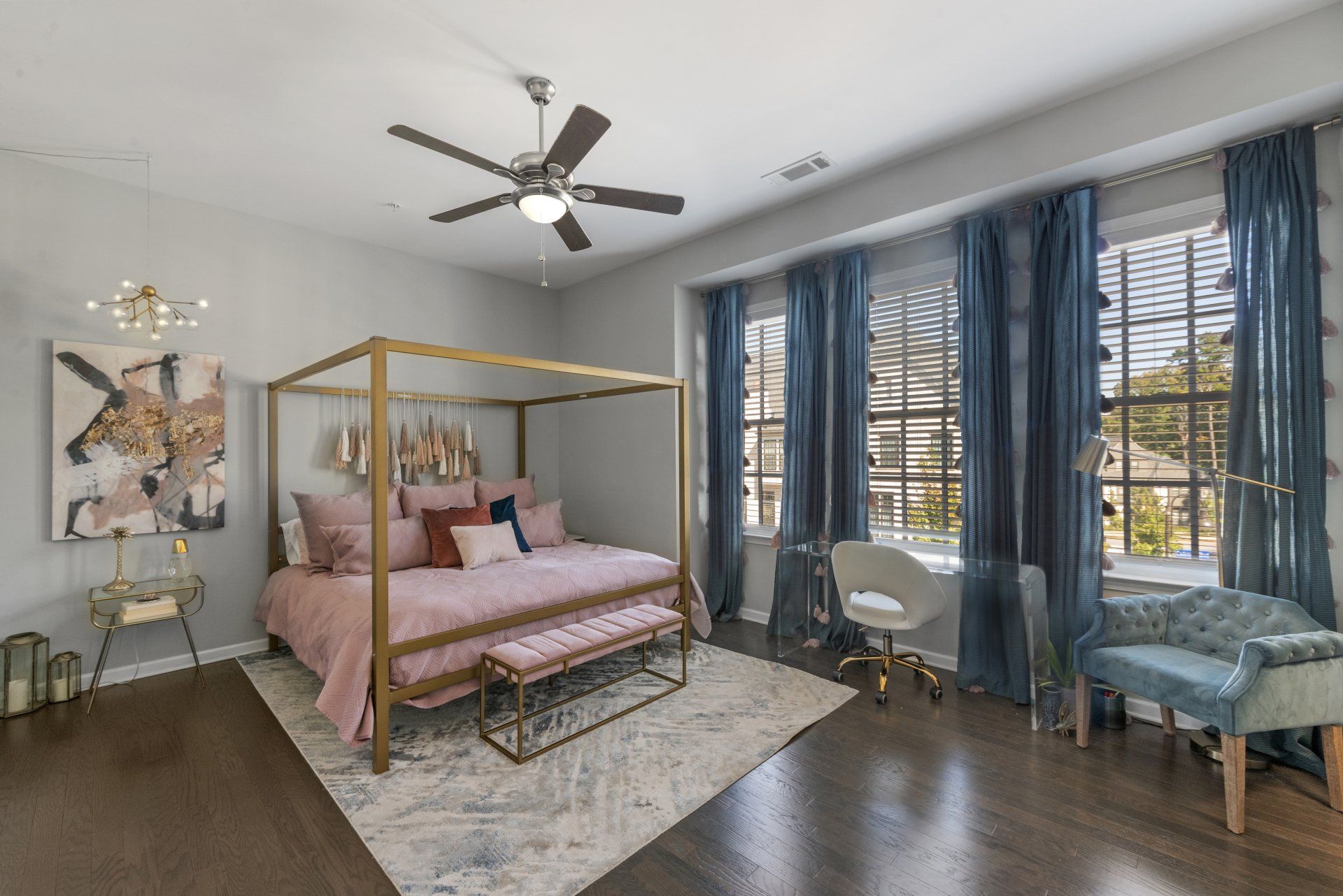 Bedroom with a gold canopy bed, pink bedding, blue curtains, and a desk by a window.