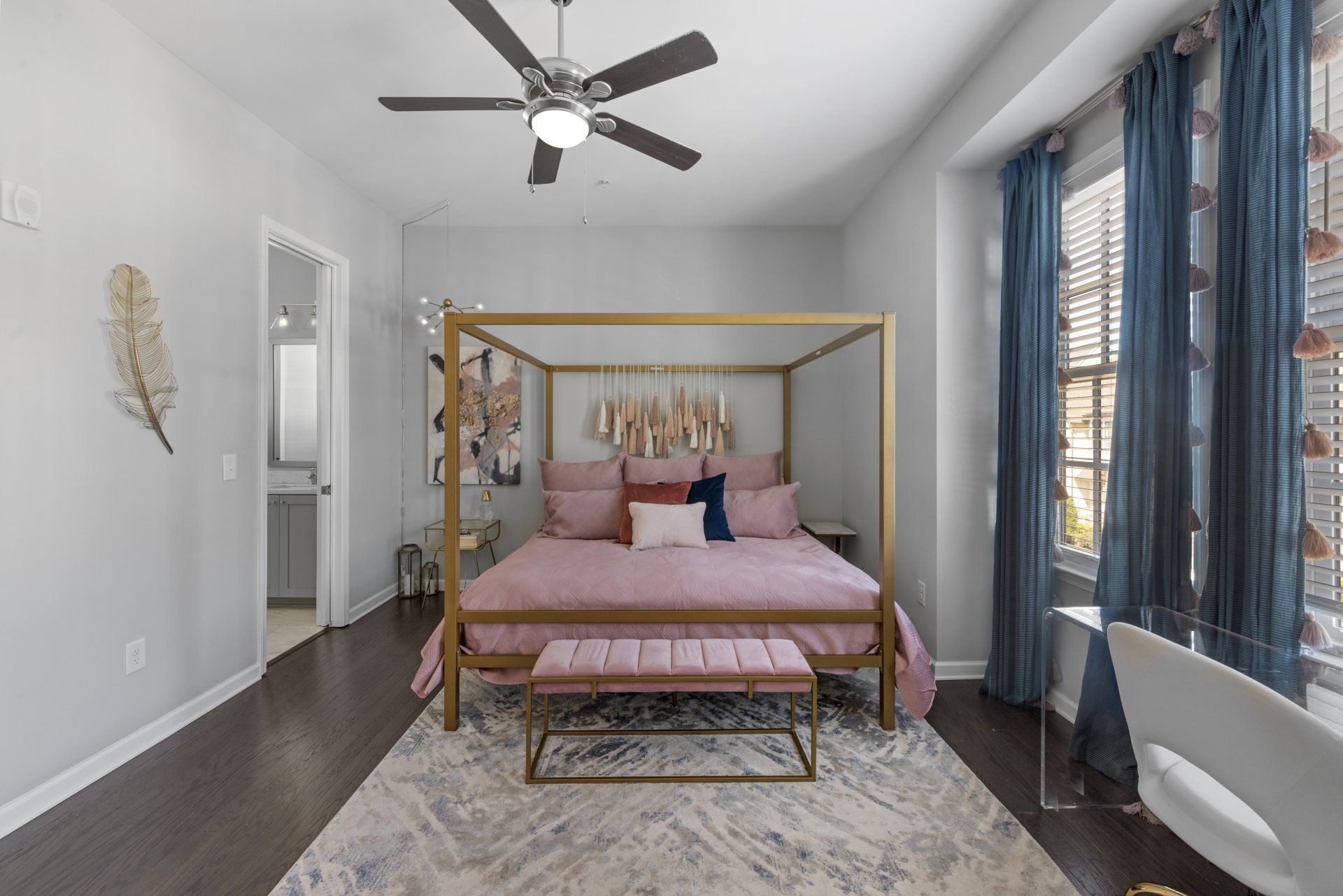Bedroom with gold canopy bed, pink bedding, and a desk near window with blue curtains.