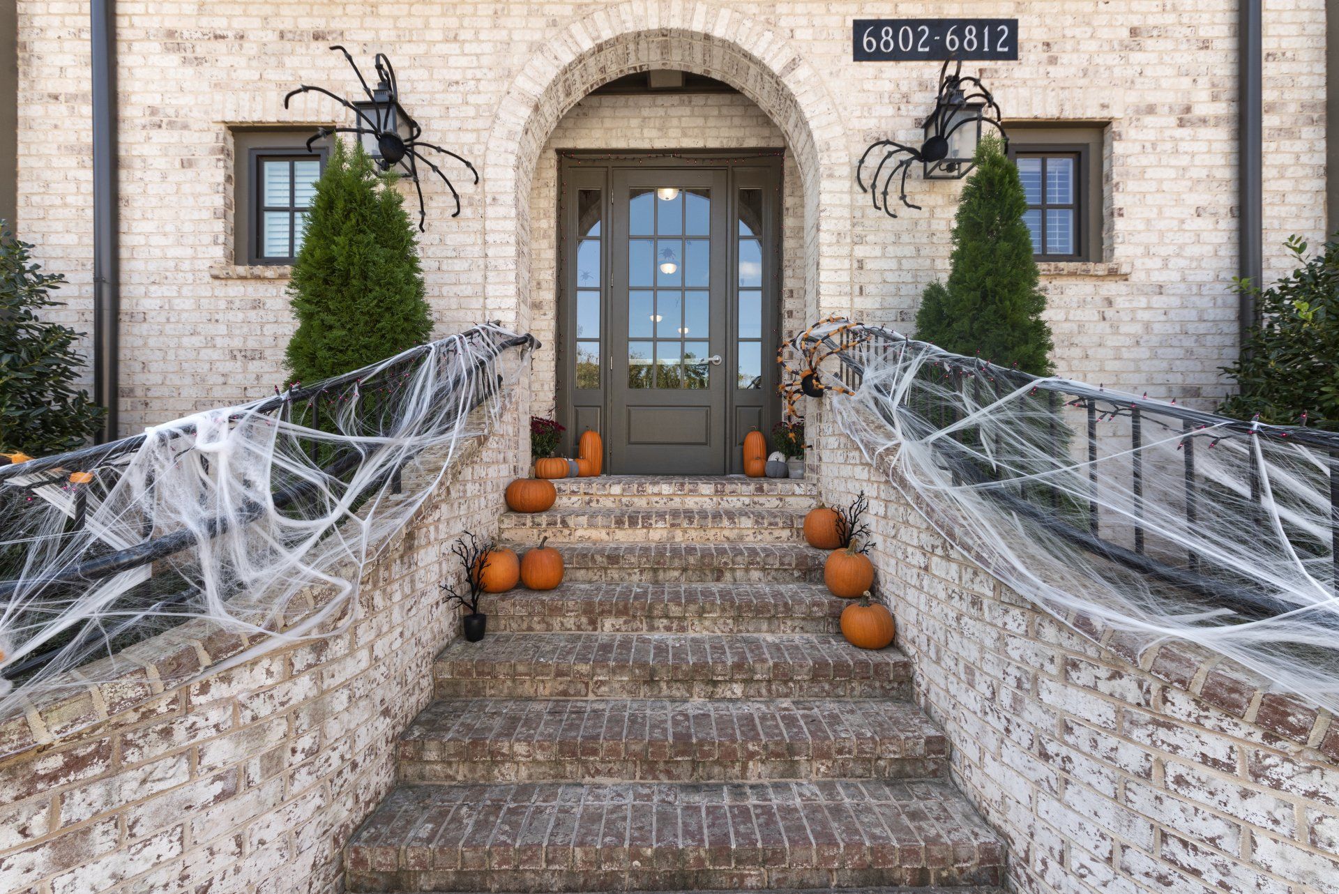 Halloween-decorated brick house with spiderwebs, pumpkins, and spiders on the porch and steps.
