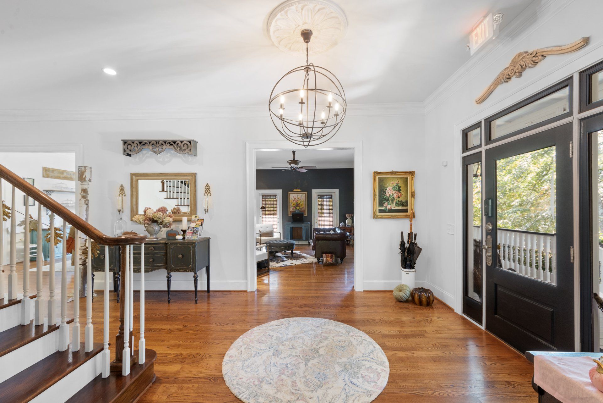 Bright entryway with chandelier, dark doors, and a round rug on a wood floor.