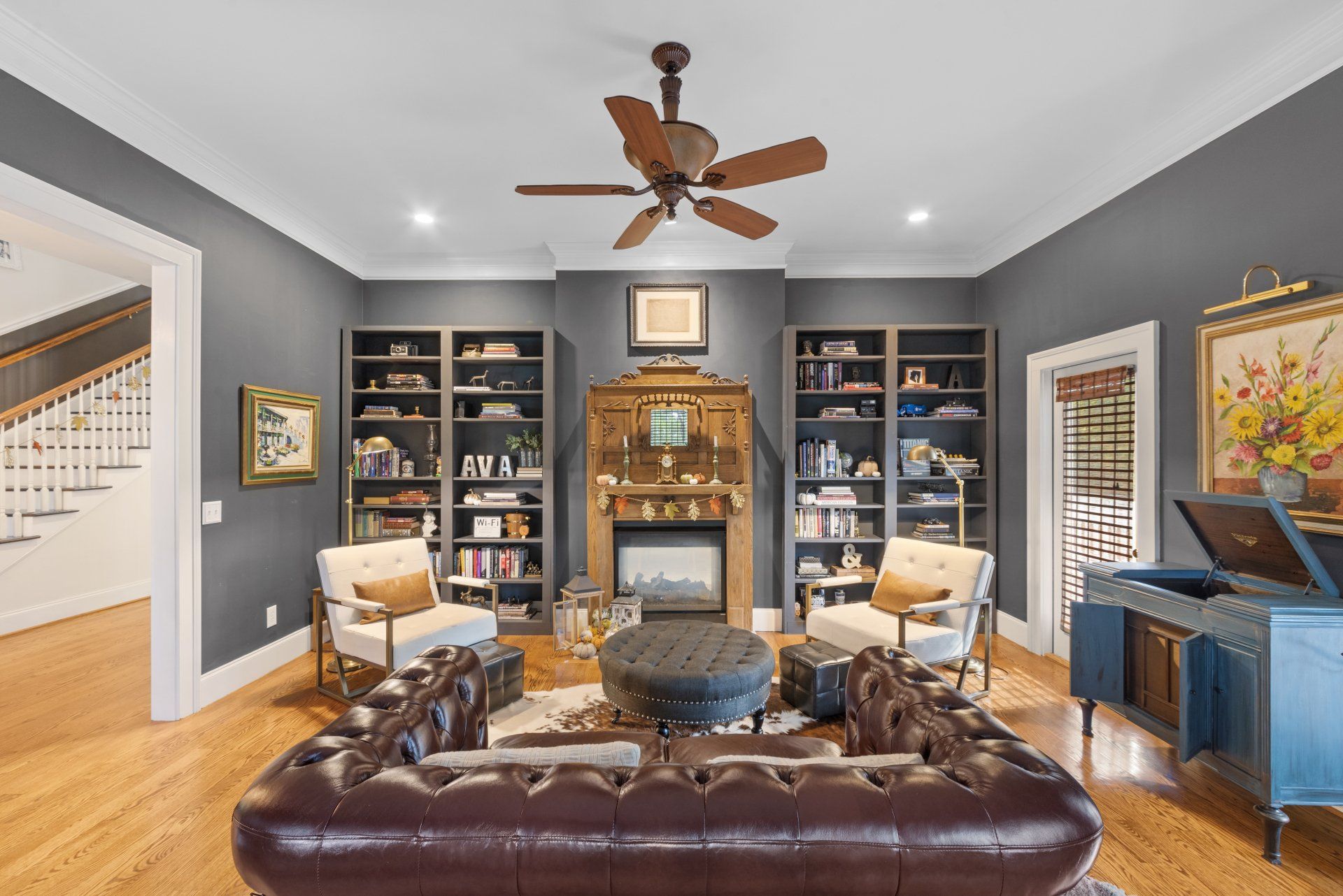 Living room with fireplace, bookshelves, leather sofa, armchairs, and record player.