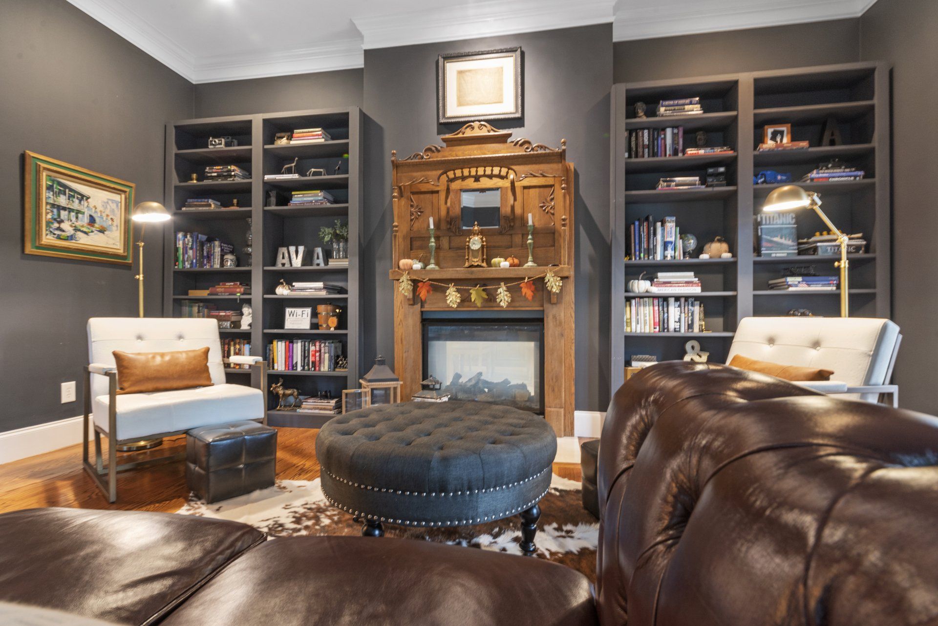 Cozy living room with fireplace, bookshelves, armchairs, and leather sofa, dark walls, and ornate wood features.