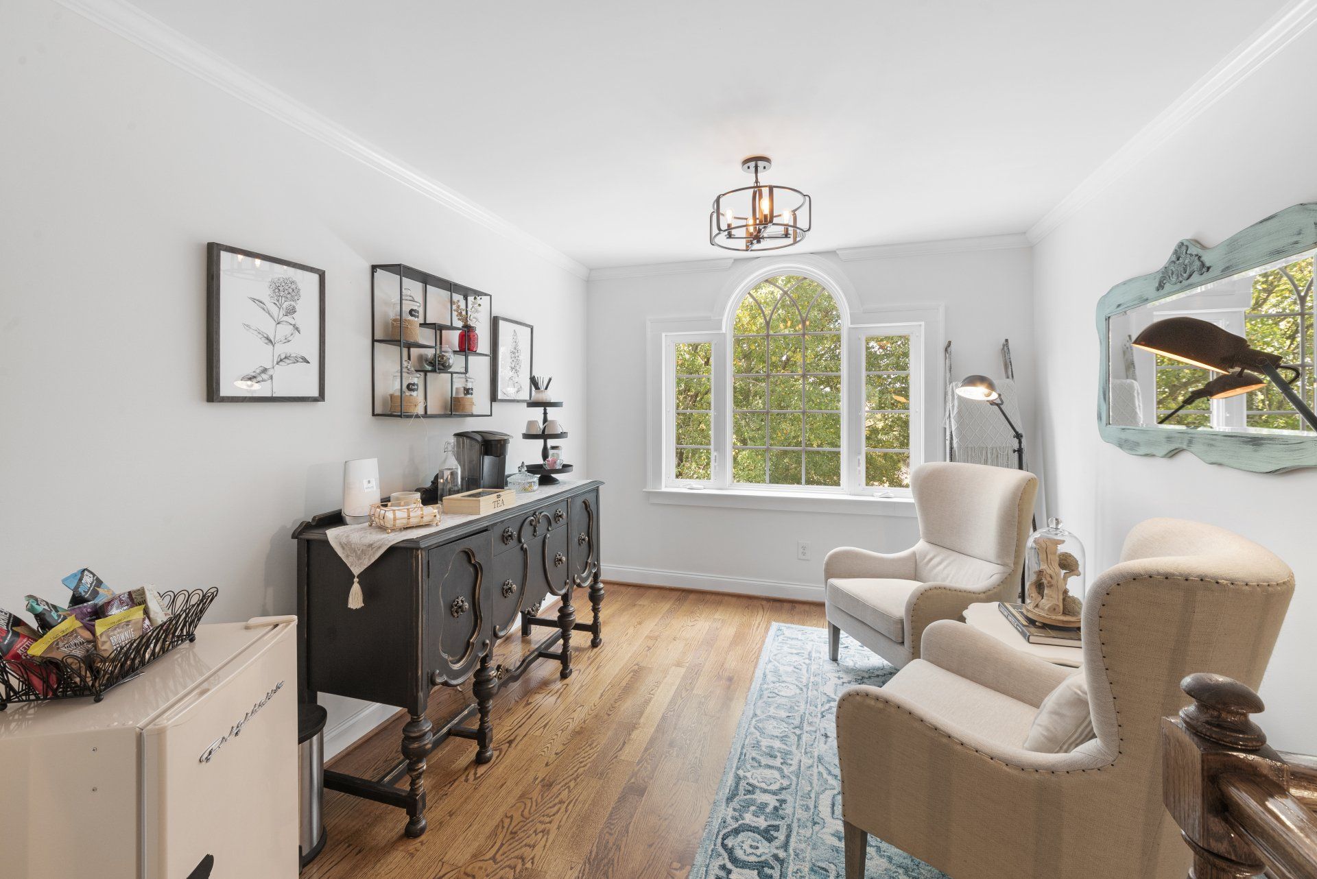 Cozy room with antique furniture, coffee bar, and two armchairs facing a large arched window.
