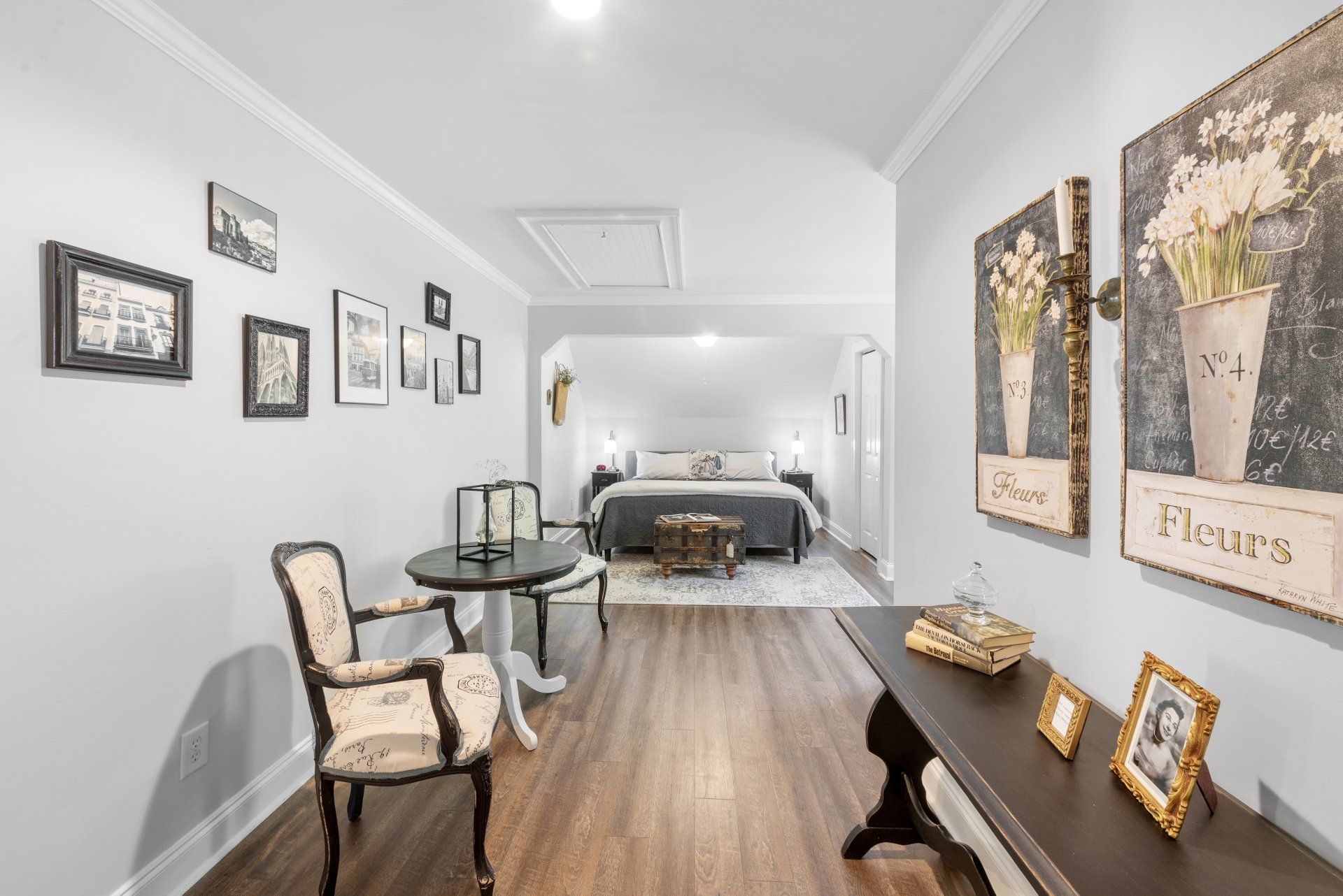 Hallway with dark wood flooring, seating area, and framed art leading to a bedroom with a bed.