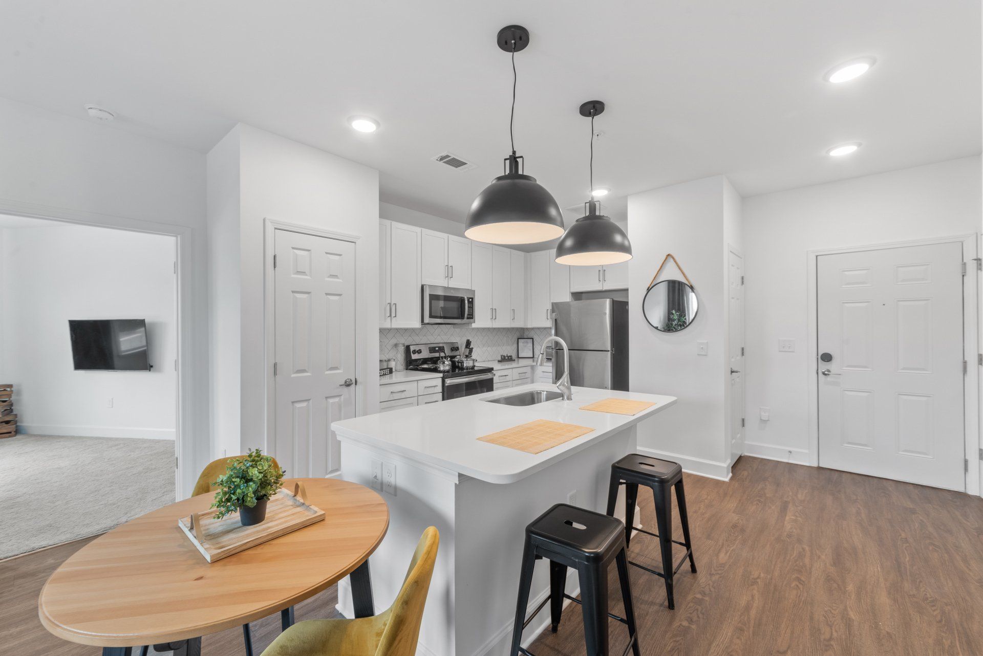 Modern kitchen with white cabinets, island, and dining area. Black pendant lights, stools, and round table.