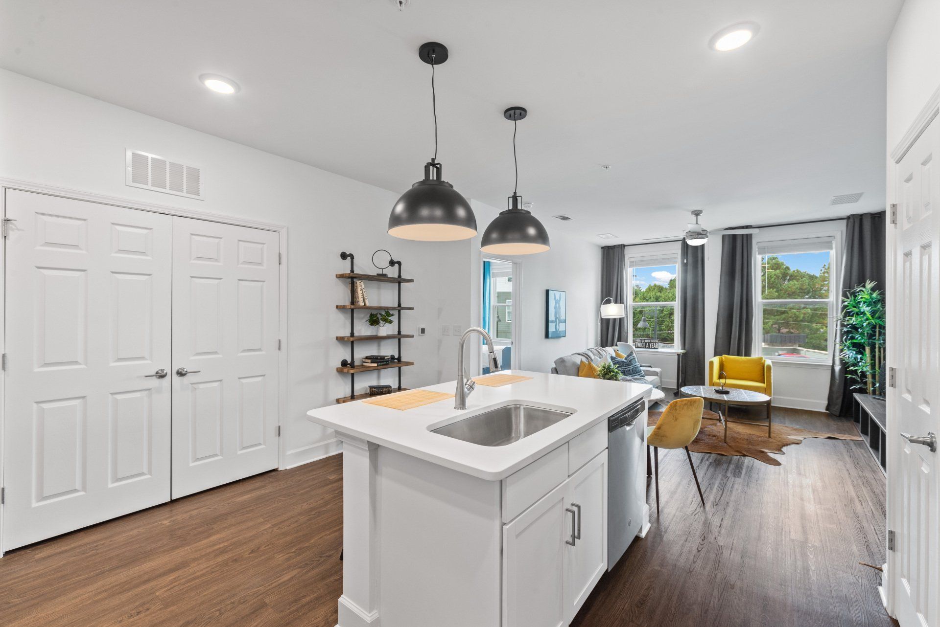 Modern kitchen with island, pendant lights, and living room in background; white and wood tones.