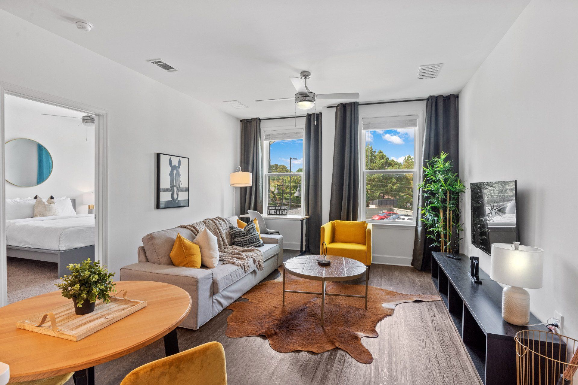 Living room with gray sofa, yellow chair, round table, TV, and large windows.