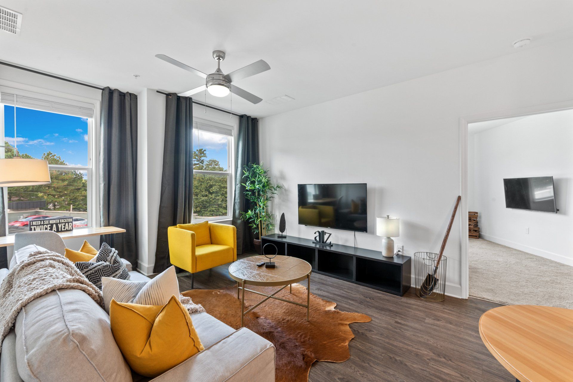 Living room with white walls, TV, yellow chair, brown rug, and windows.
