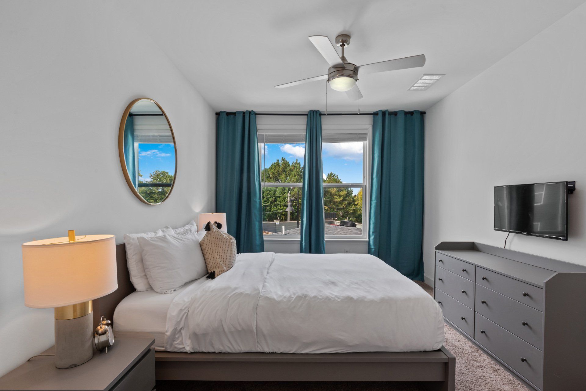 Bedroom with bed, dresser, teal curtains, and a ceiling fan.