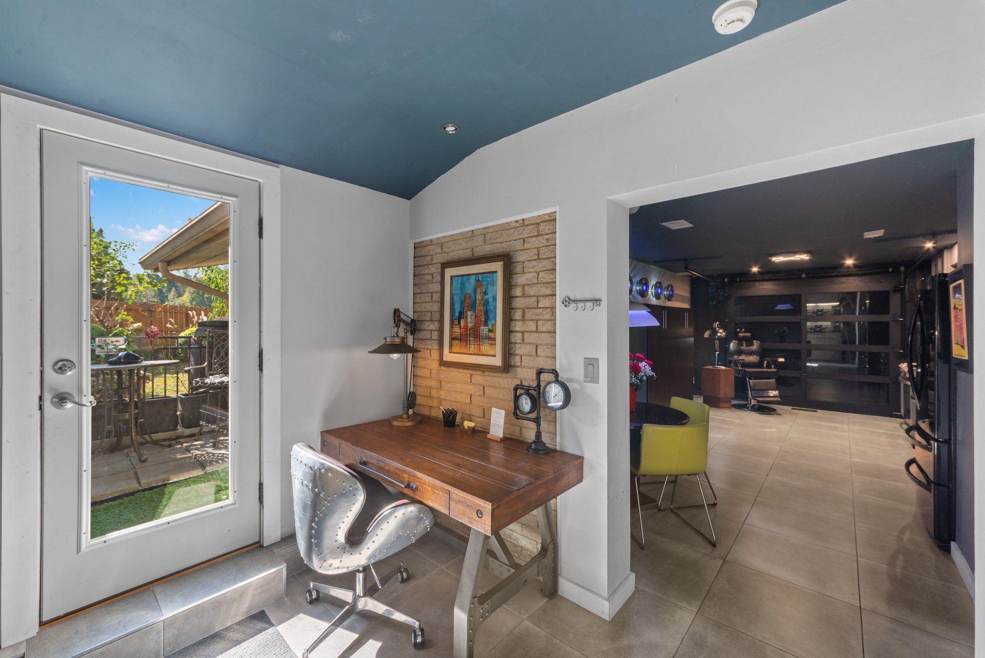 Home office with a desk, chair, and door leading outside, adjacent to a room with entertainment systems.