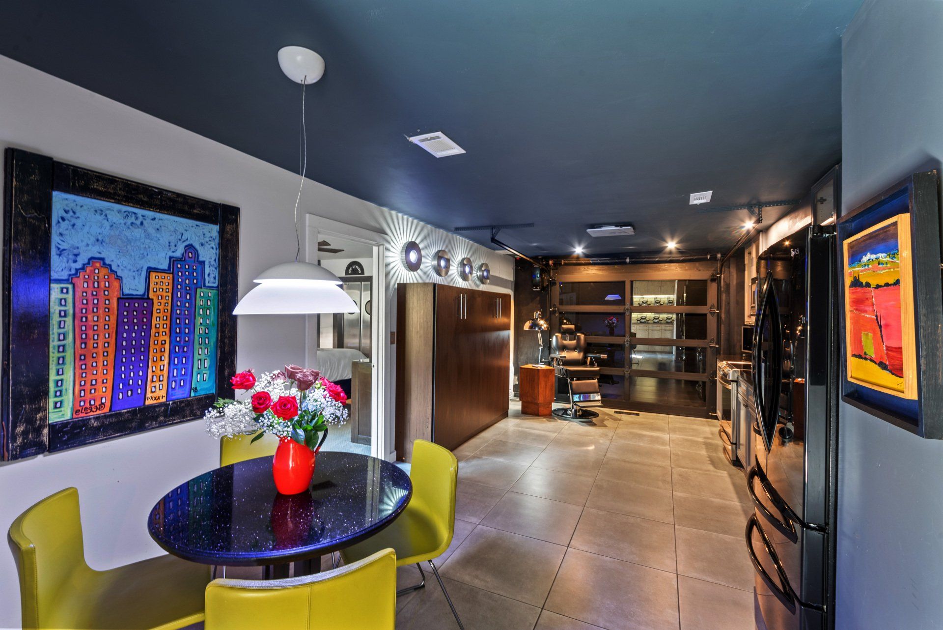 Dining area with yellow chairs, a dark round table, cityscape art, and a dark blue ceiling.