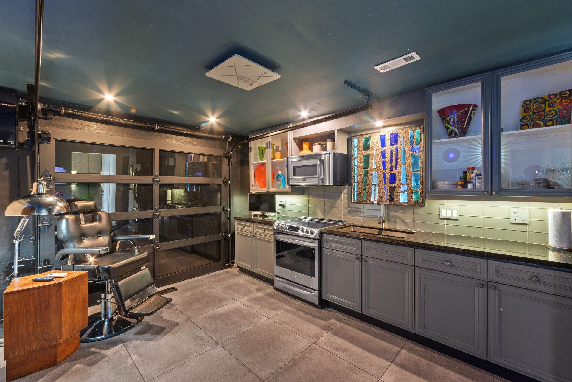 Modern industrial kitchen with gray cabinets, stainless steel appliances, and a glass garage door.