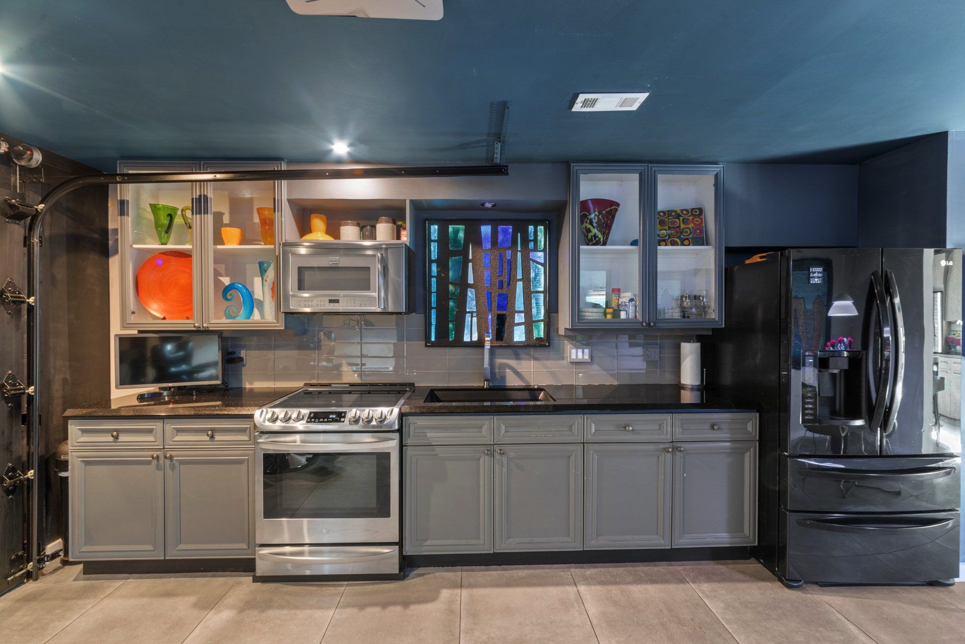 A garage kitchen with gray cabinets, a stainless steel stove, and a black refrigerator.