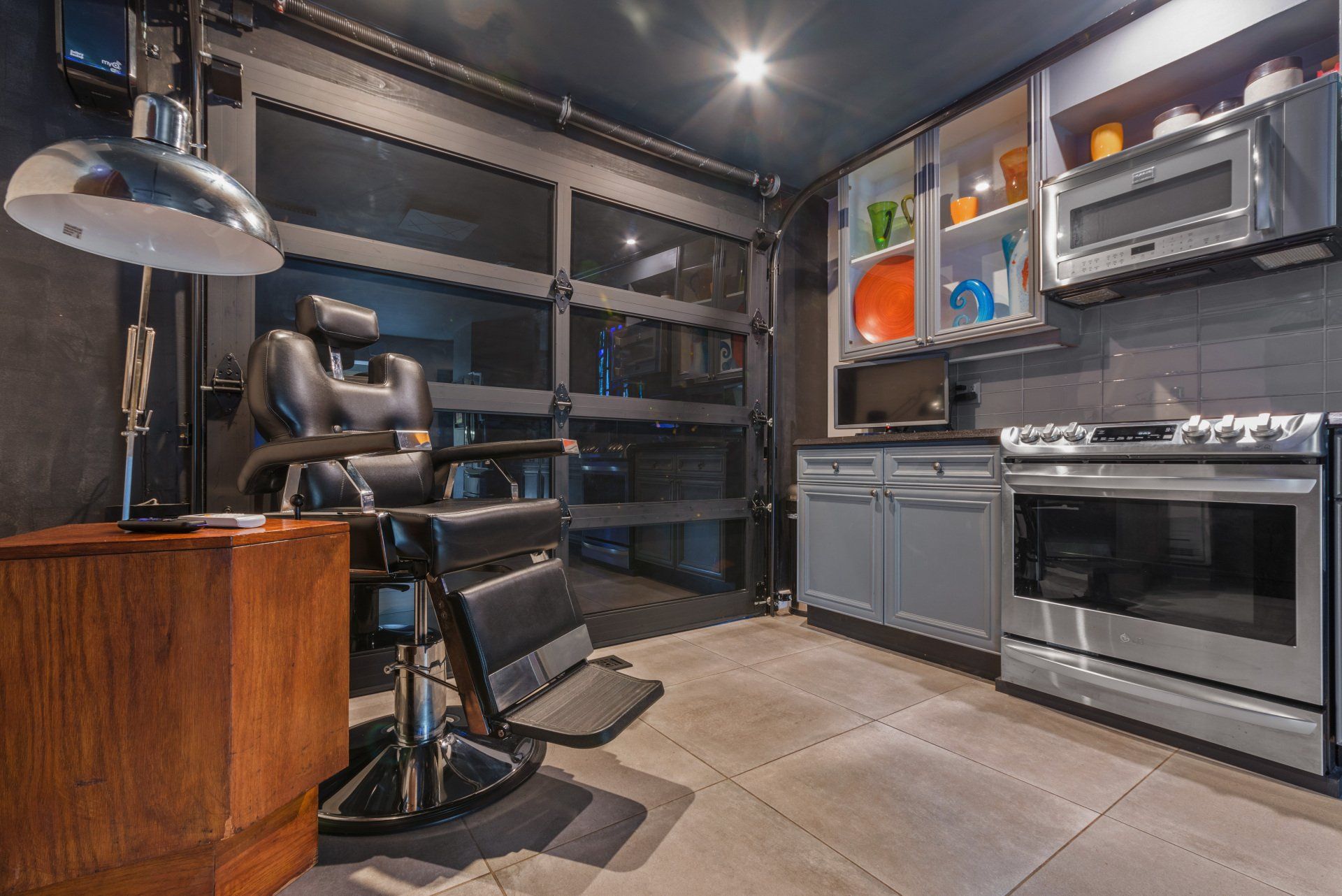 A renovated garage space with a barber chair, kitchenette, and a glass garage door.