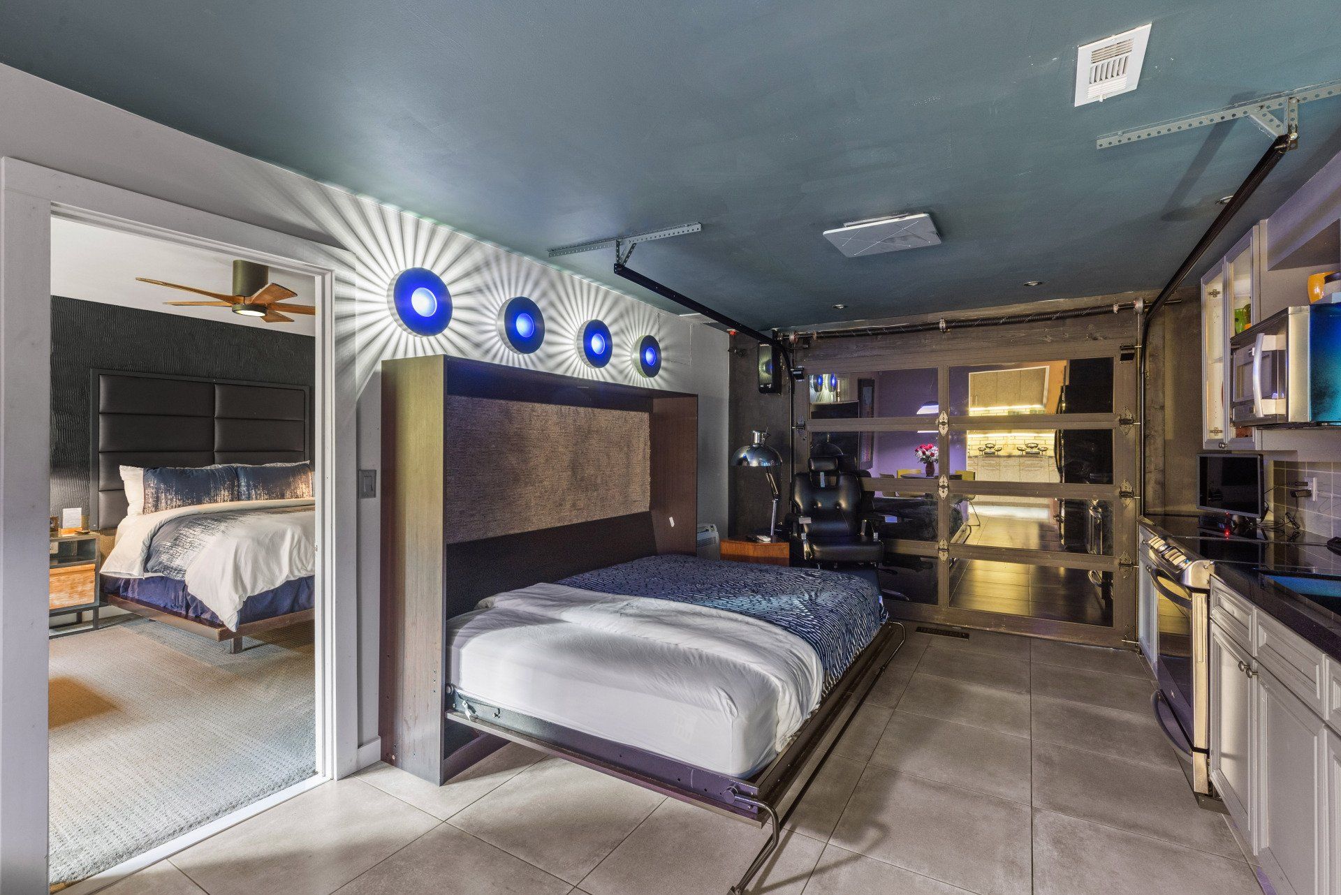 Modern studio apartment with a fold-down bed, mirror, and a small kitchen area.