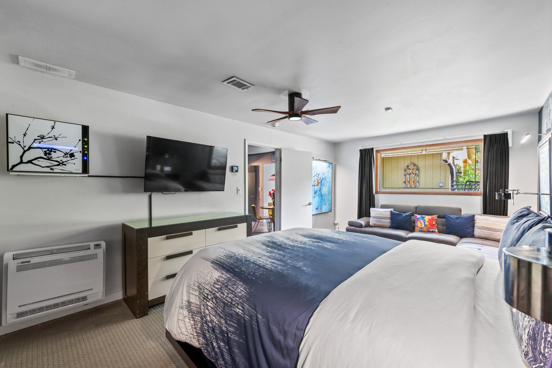Bedroom with a king-size bed, dresser, large TV, and a window with a colorful view.