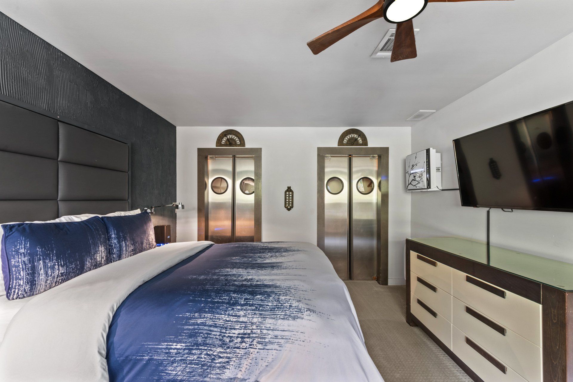Bedroom with a large bed, TV, dresser, and two elevator doors.