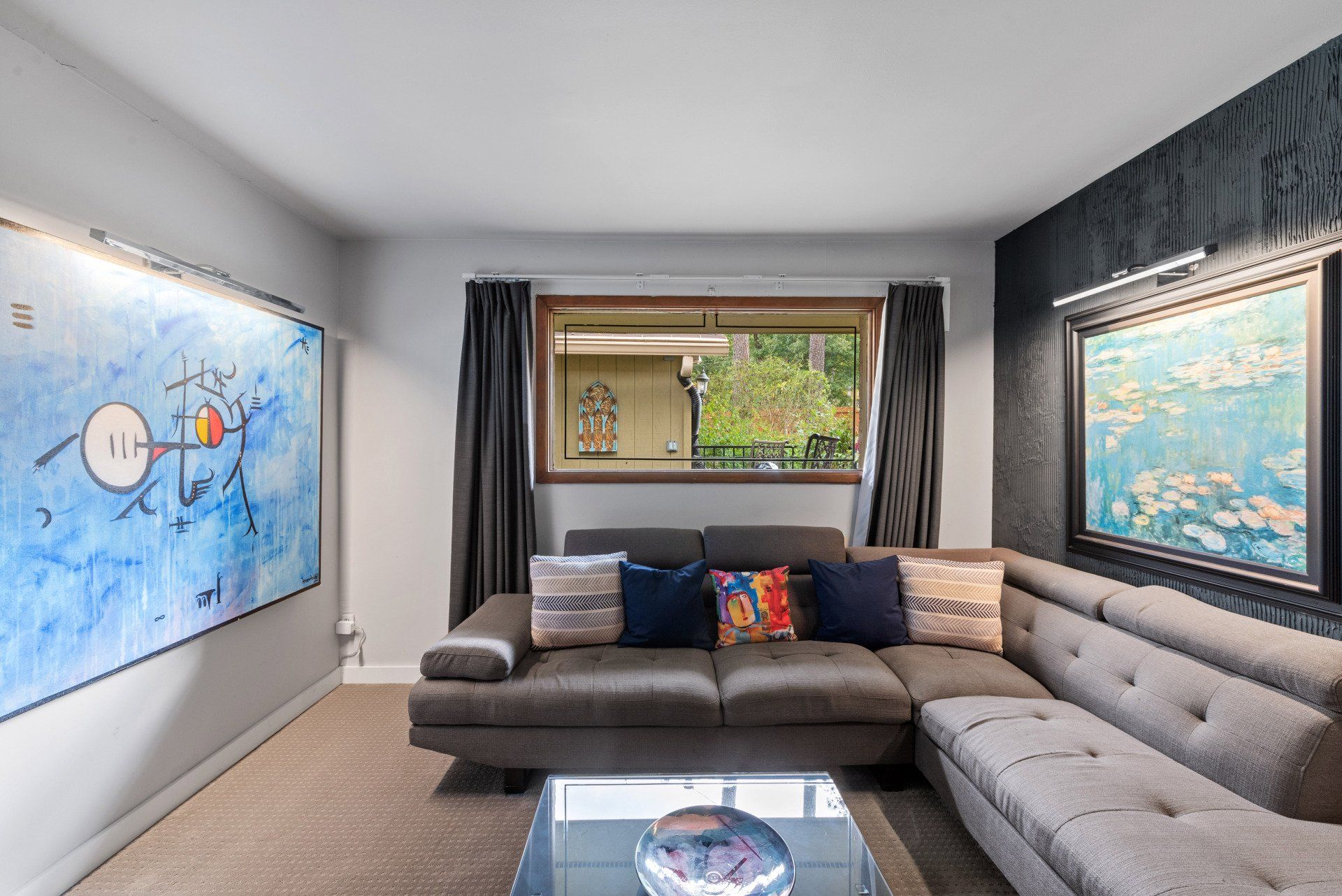 Cozy living room with gray sectional sofa, art on walls, glass coffee table, and a window.