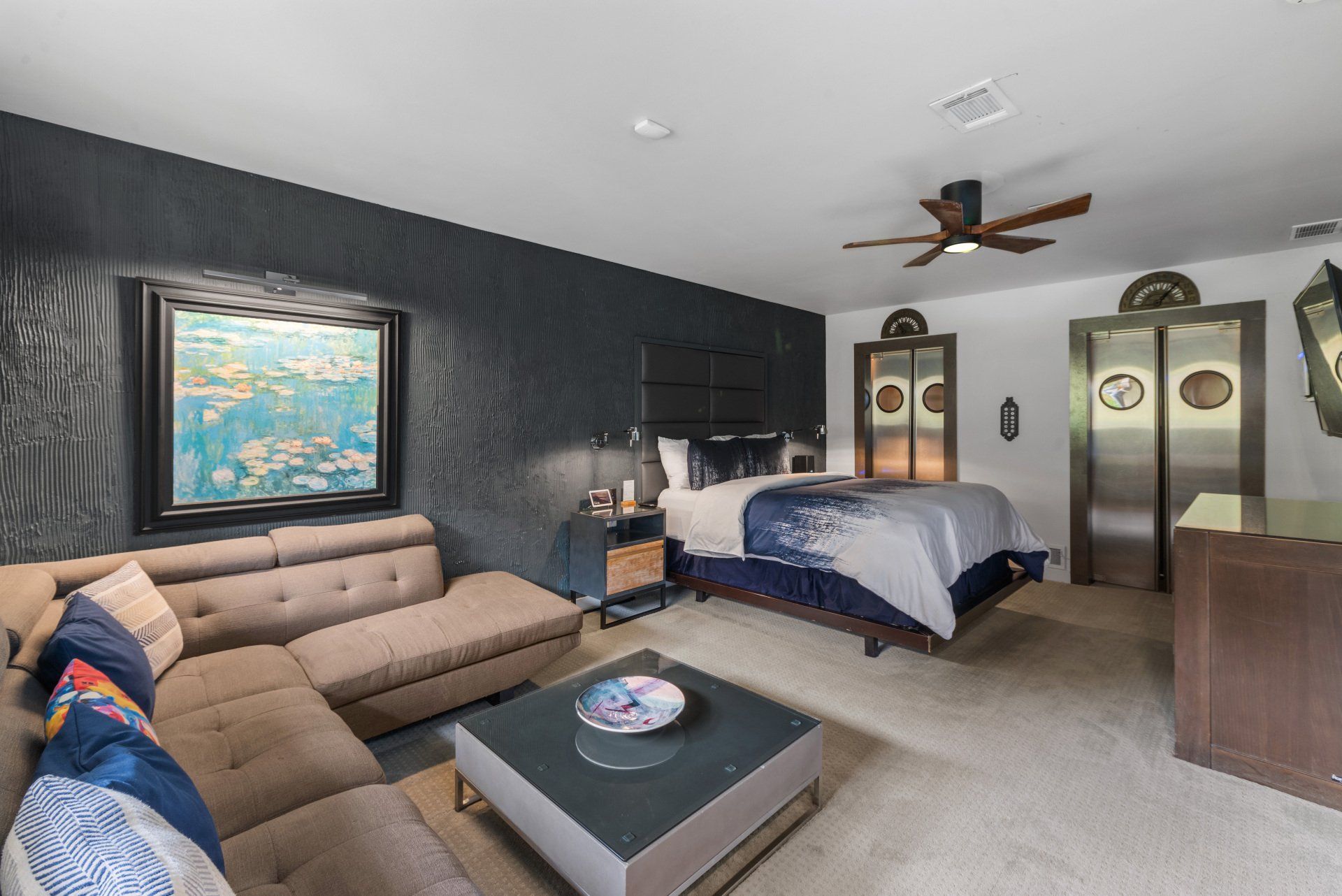 Spacious hotel room with a dark accent wall, sectional sofa, bed, and modern decor.