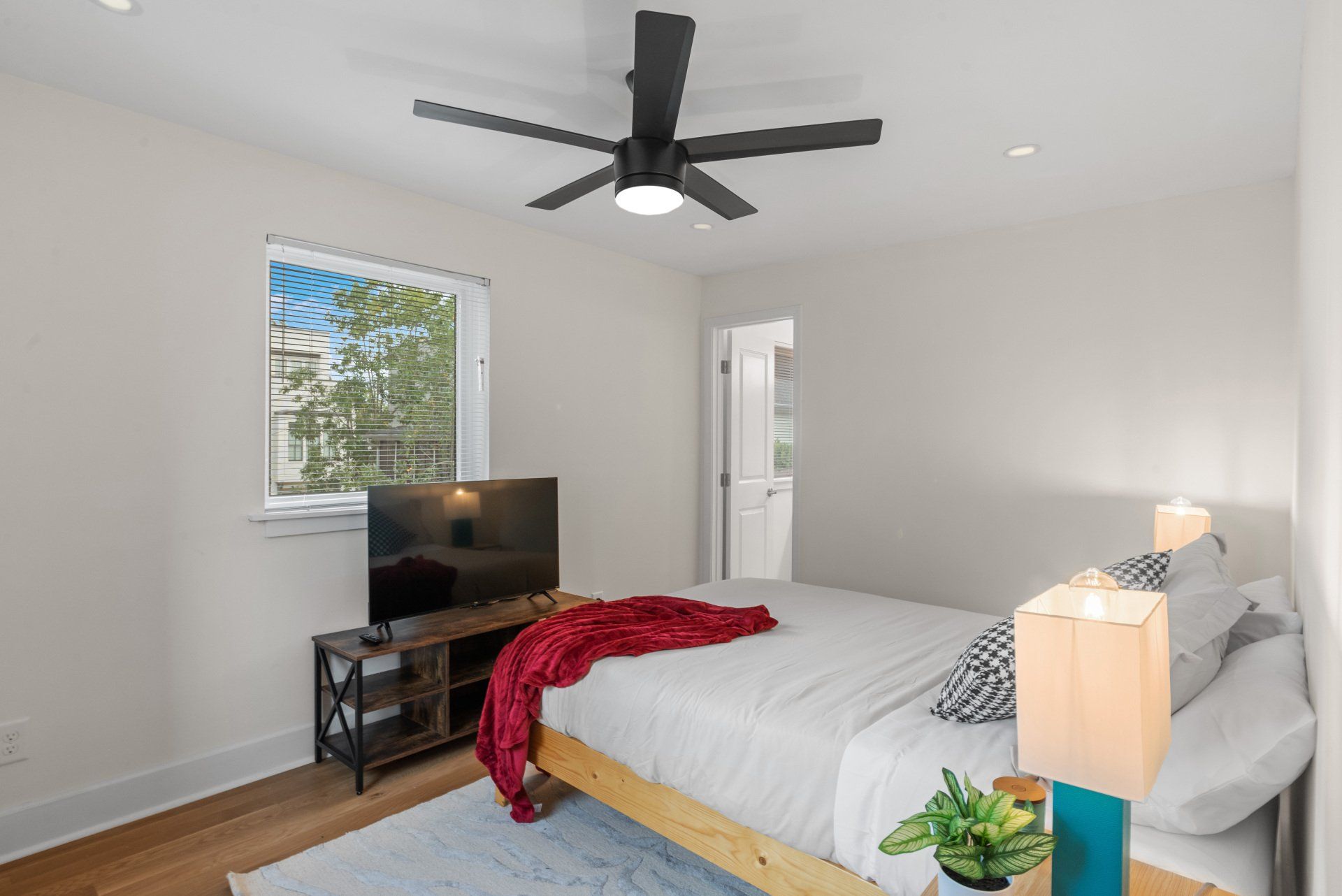 Bedroom with bed, TV, window, ceiling fan, and wooden floor.