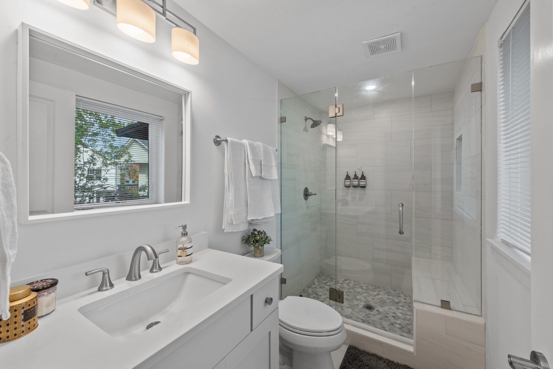White bathroom with vanity, glass shower, and toilet.