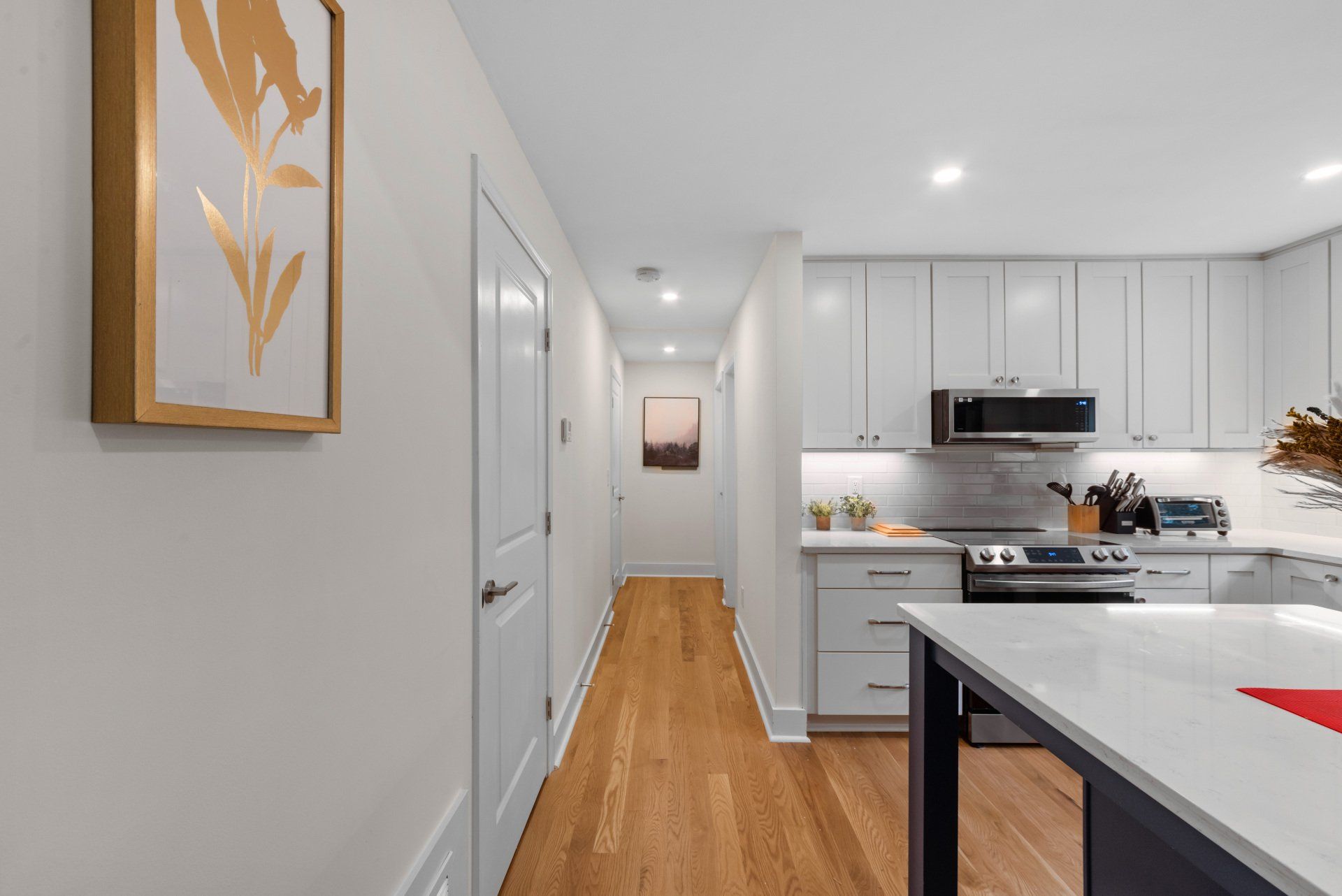 Hallway leading to kitchen, wood floors, white walls, light gray cabinets, quartz countertops.