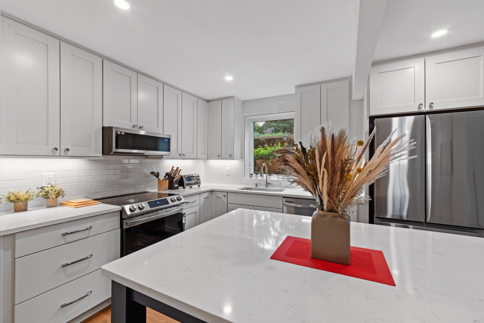 Modern kitchen with white cabinets, stainless steel appliances, island, and window.