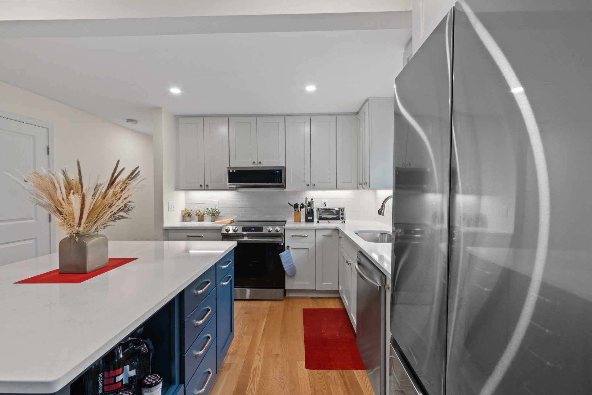 Modern kitchen with white countertops, blue island, and stainless steel appliances.