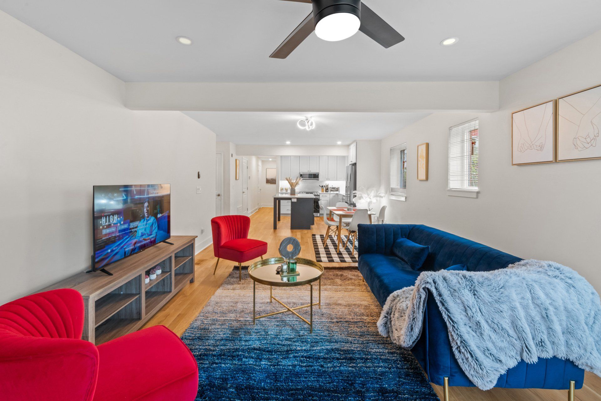 Living room with blue sofa, red chairs, TV, and open view to kitchen.
