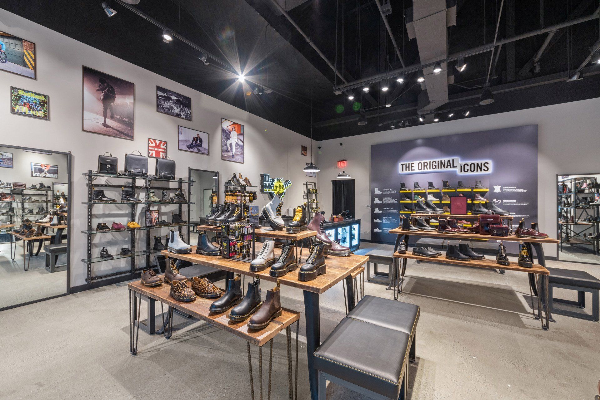 Shoe store interior with boots displayed on tables and shelves. Artwork and a large logo are on the walls.
