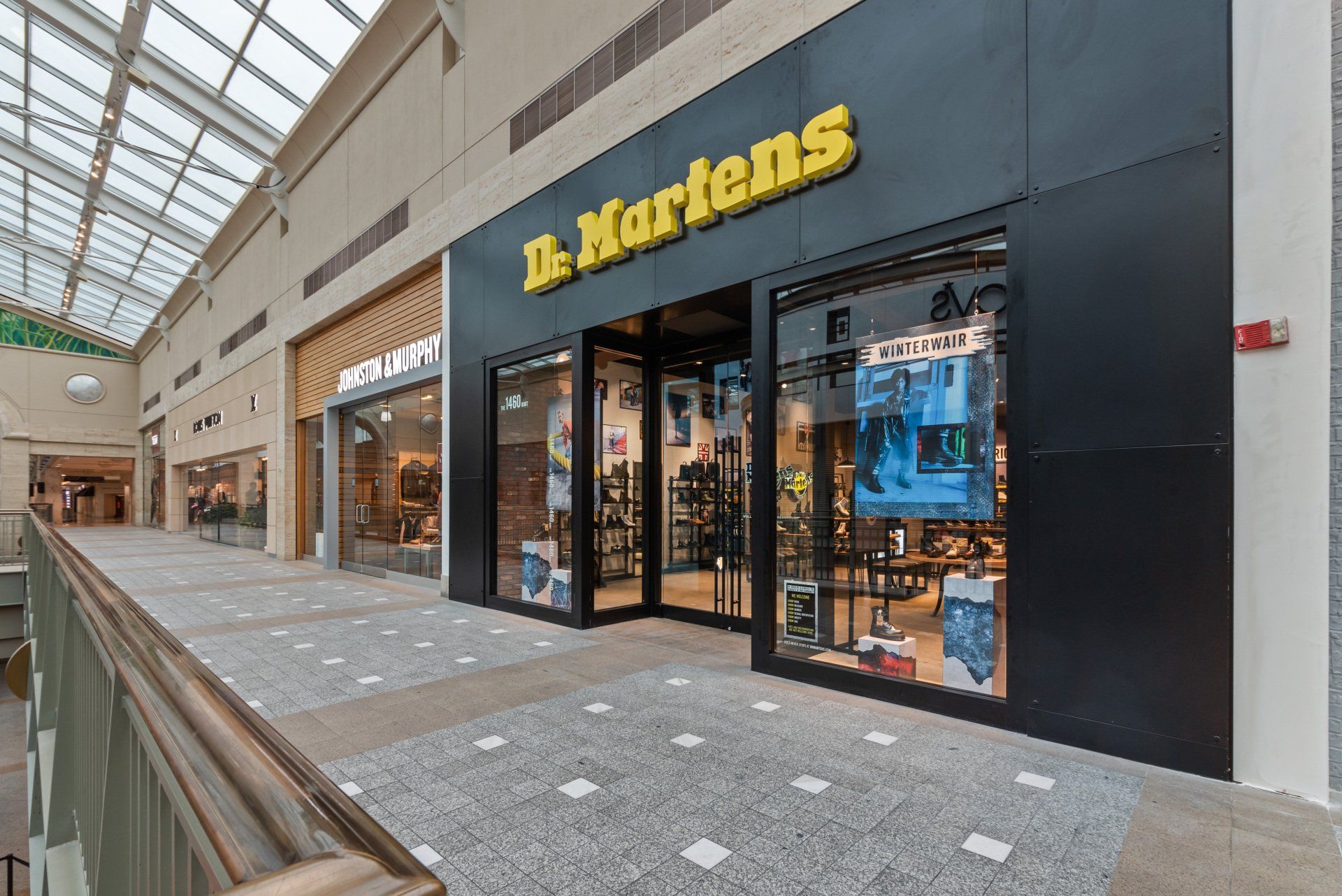 Dr. Martens store entrance in a mall. Black facade with yellow logo. Glass doors and windows.