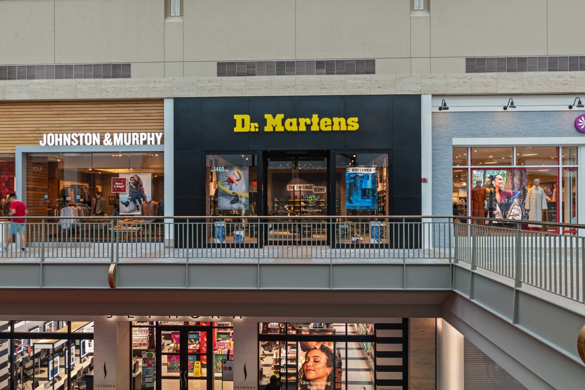 Dr. Martens storefront in a mall, black facade with yellow logo. Flanked by Johnston & Murphy and another store.
