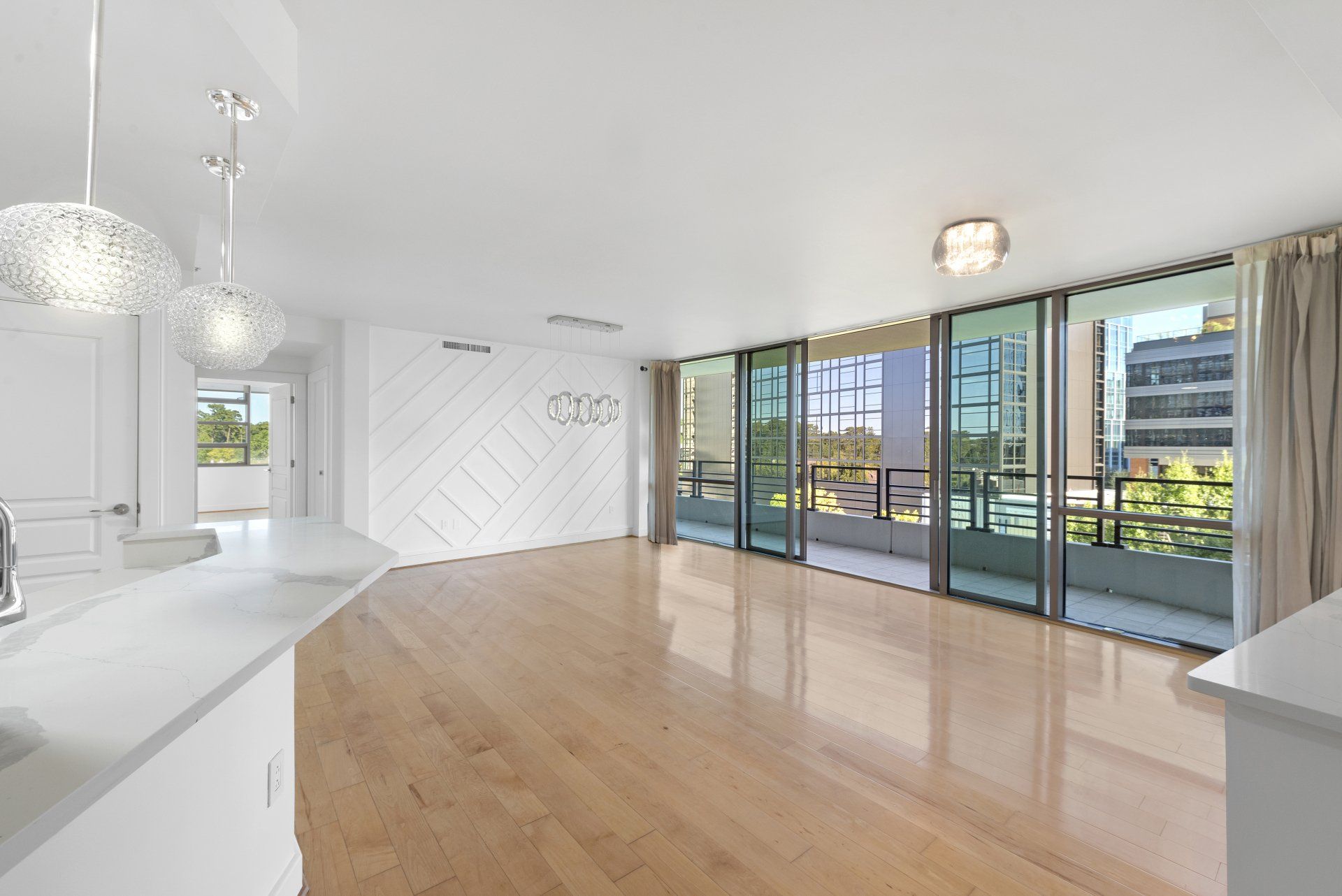 Bright, empty modern living space with light wood floors, white walls, and balcony access.