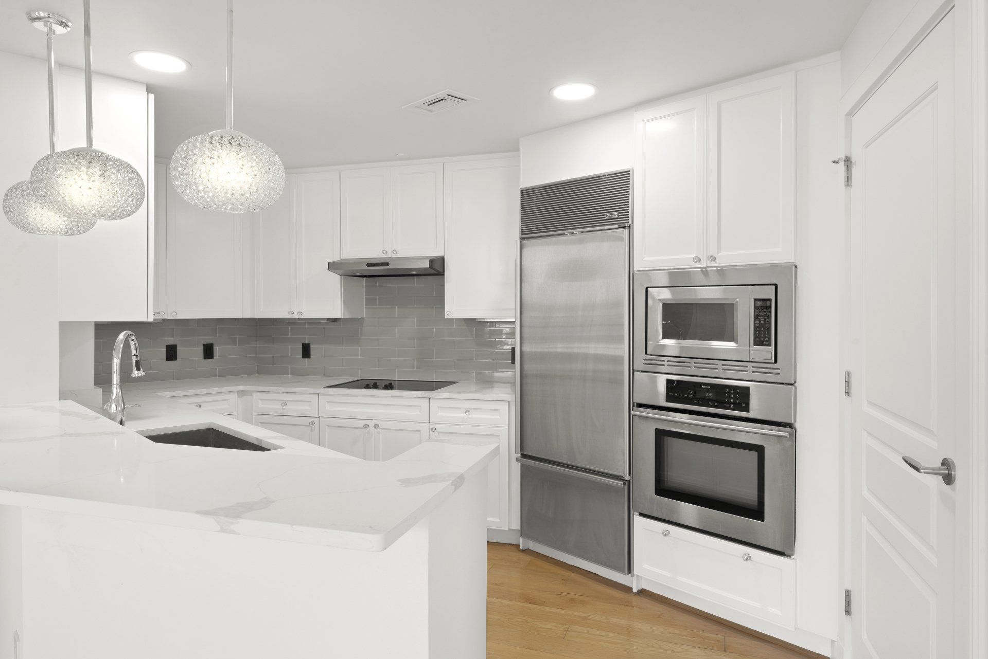 Modern white kitchen with stainless steel appliances, marble countertops, and pendant lighting.