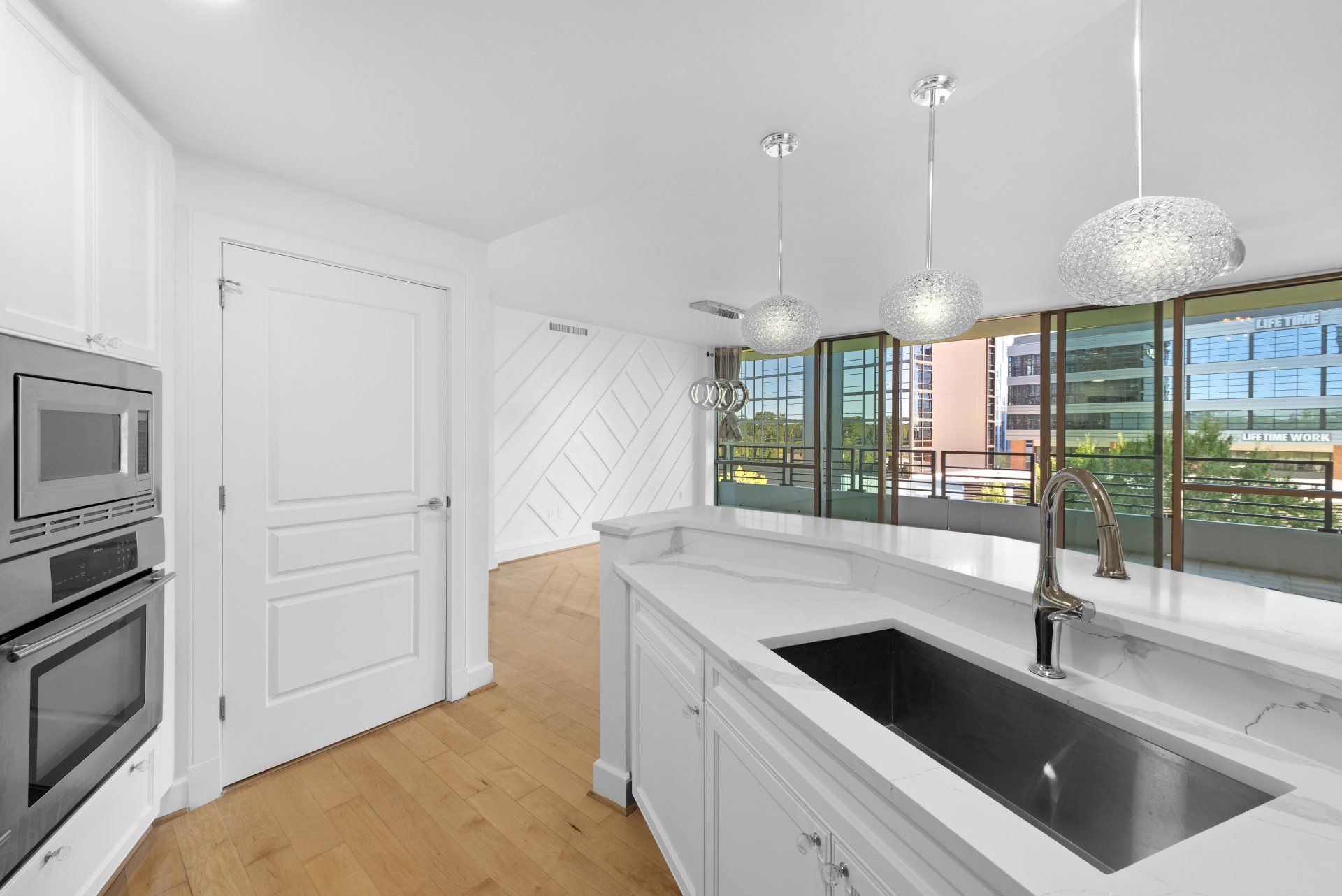 Modern white kitchen with stainless steel appliances, marble countertops, and a view.