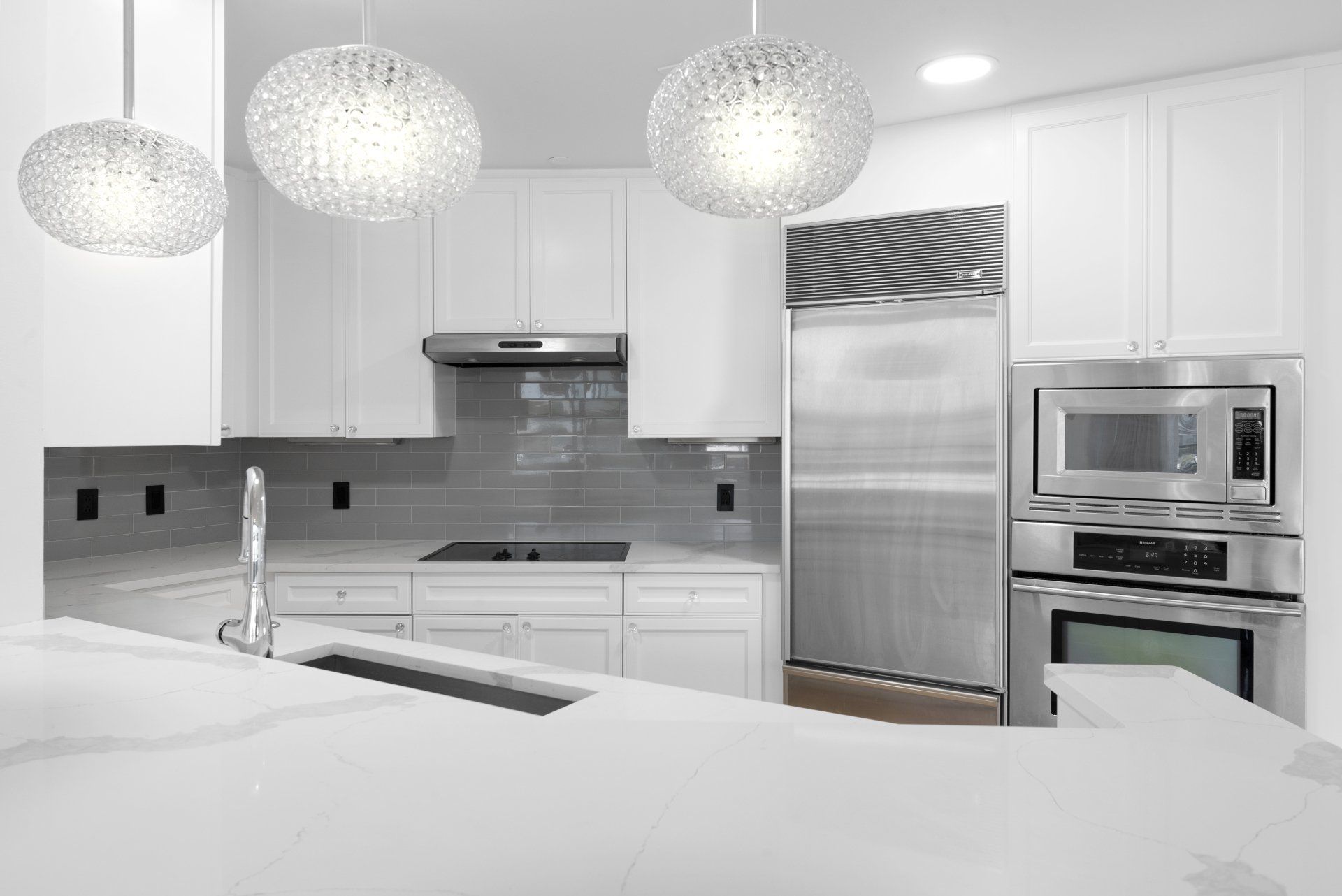 Modern white kitchen with stainless steel appliances and pendant lights.